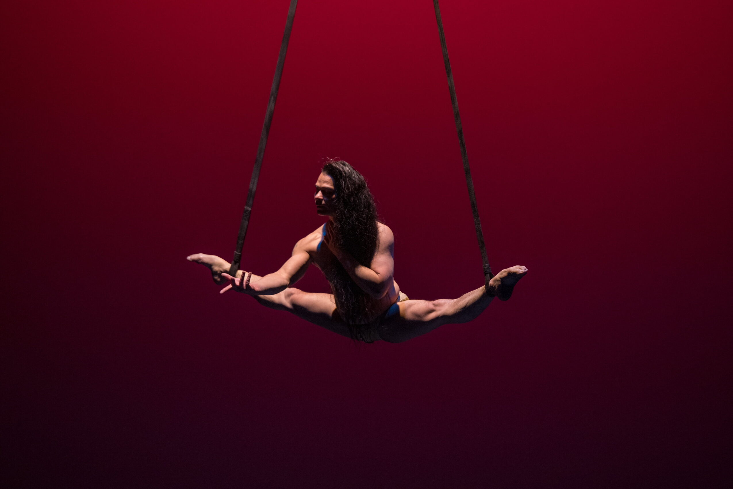 Person performing a split on a swing against a red background.