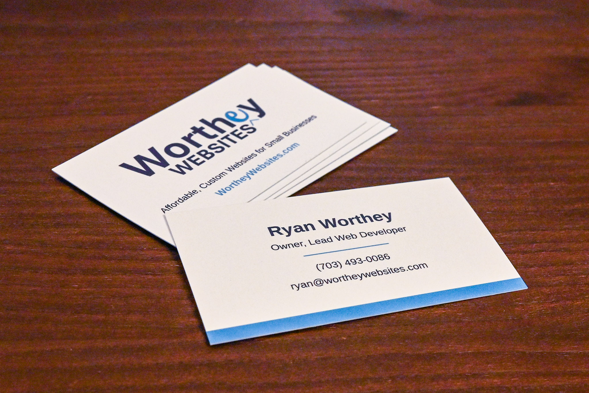 Two business cards on a wooden surface, one displaying company name and the other with contact details.