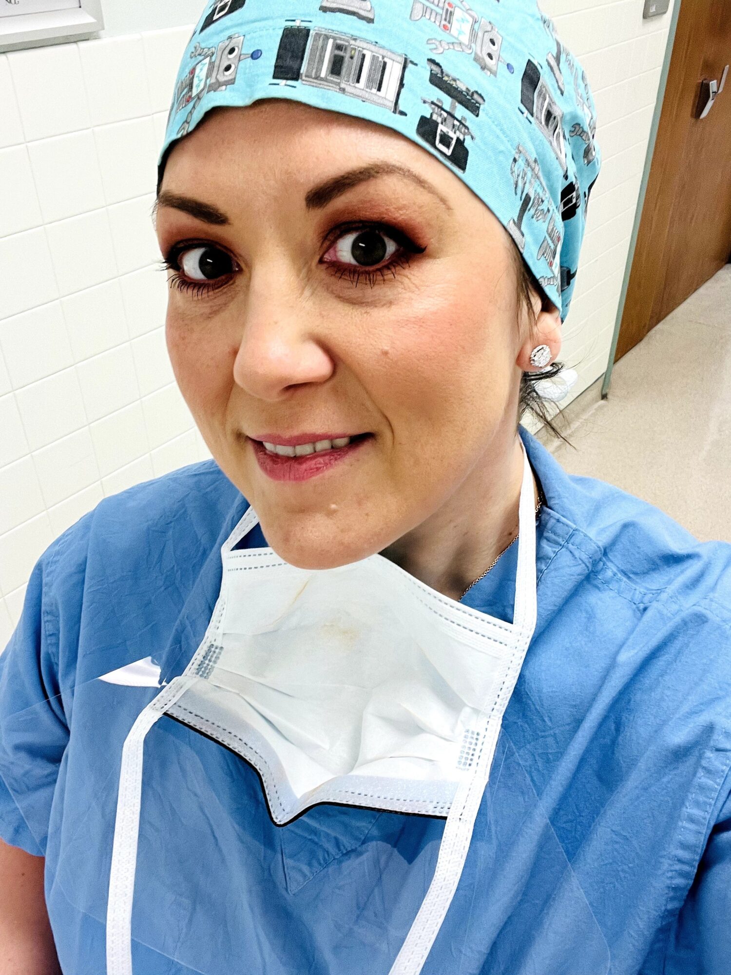Female healthcare worker in scrubs and surgical cap, smiling, in a clinical setting.
