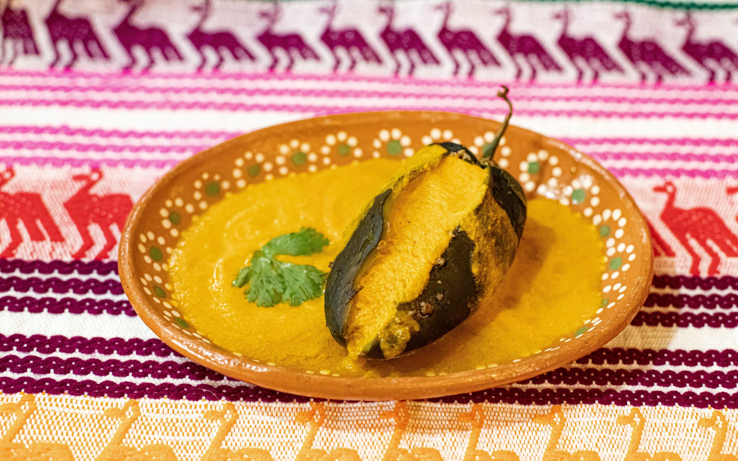A bowl with a yellow sauce and a fried eggplant slice on a colorful patterned cloth.