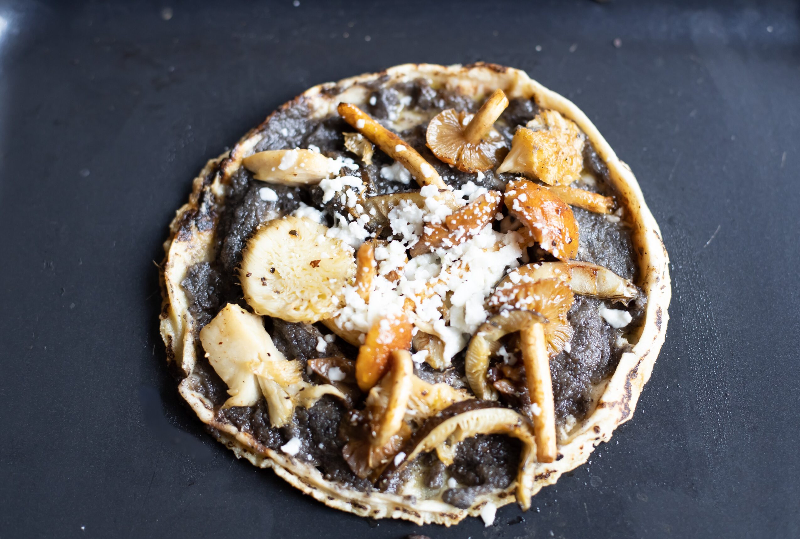 Uncooked pizza with mushrooms, cheese, and sauce on a dark surface.