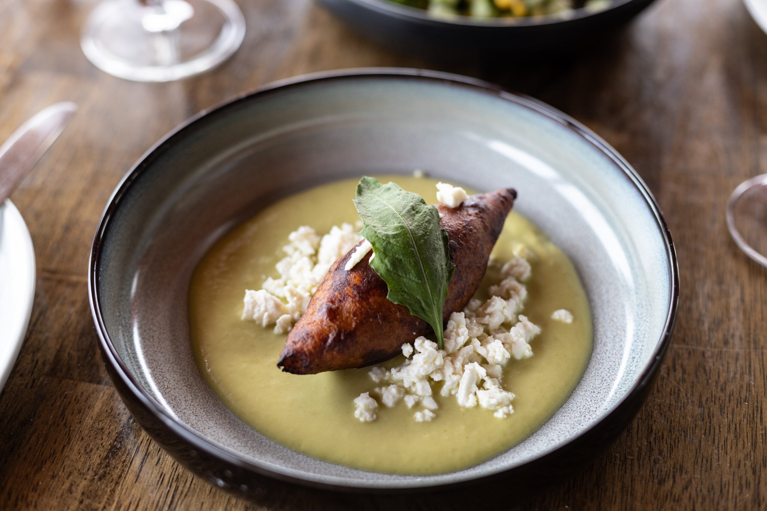 A bowl with a cooked fish fillet, garnished with a leaf, served on a bed of white crumbles and yellow sauce.