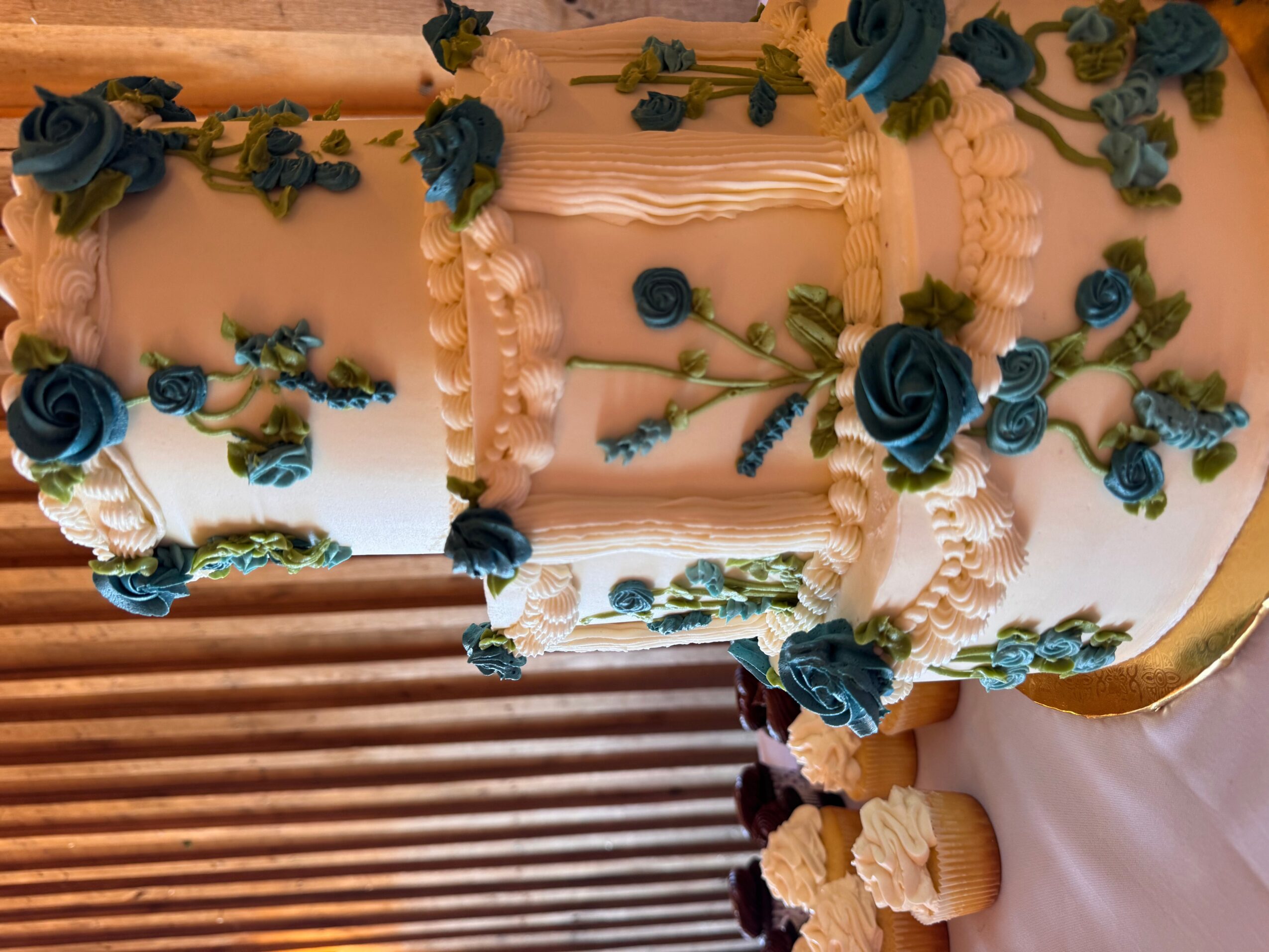 Decorated cake with blue flowers and white icing, placed on a table with a white tablecloth.