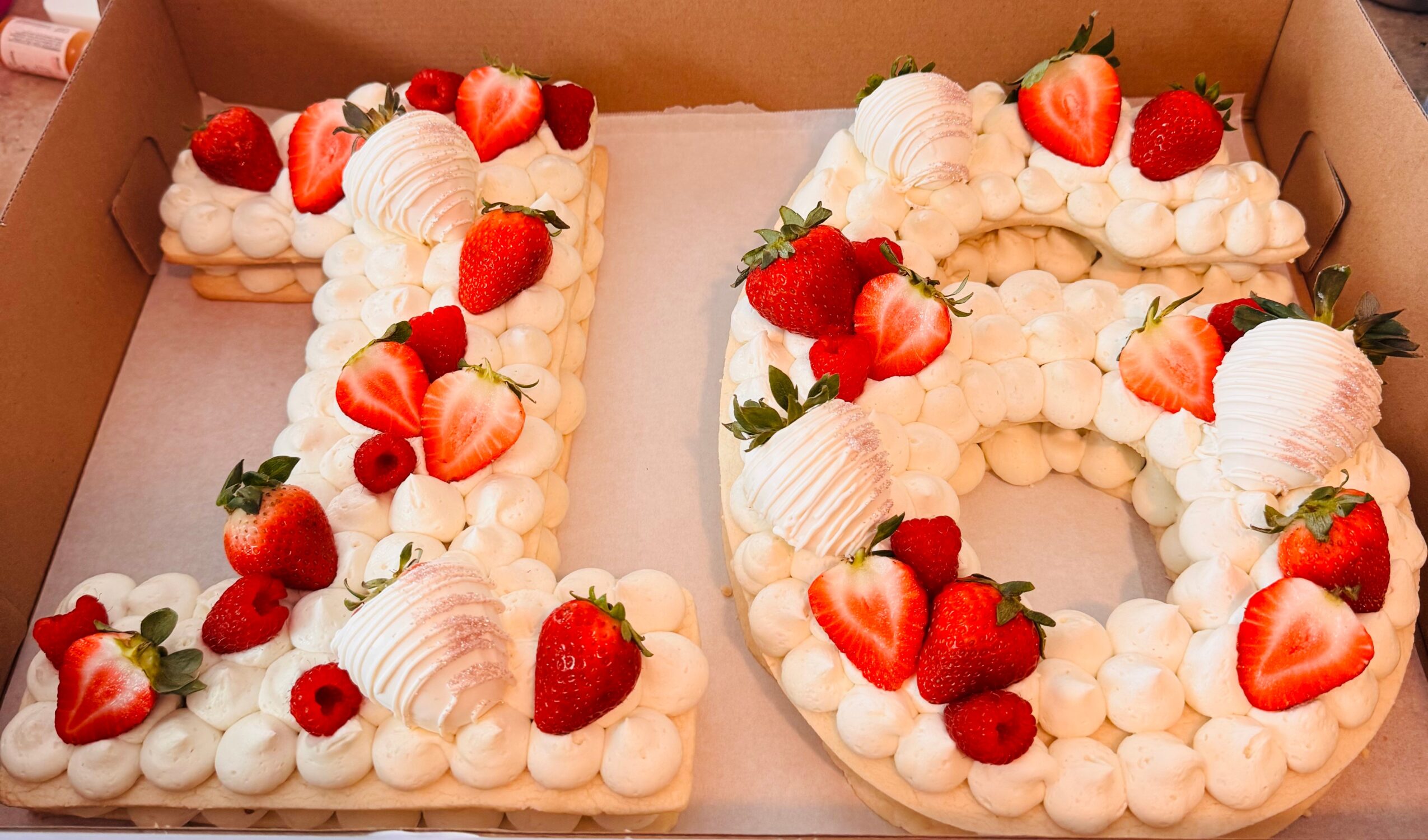 Number-shaped cake decorated with strawberries, cream, and flowers inside a box.