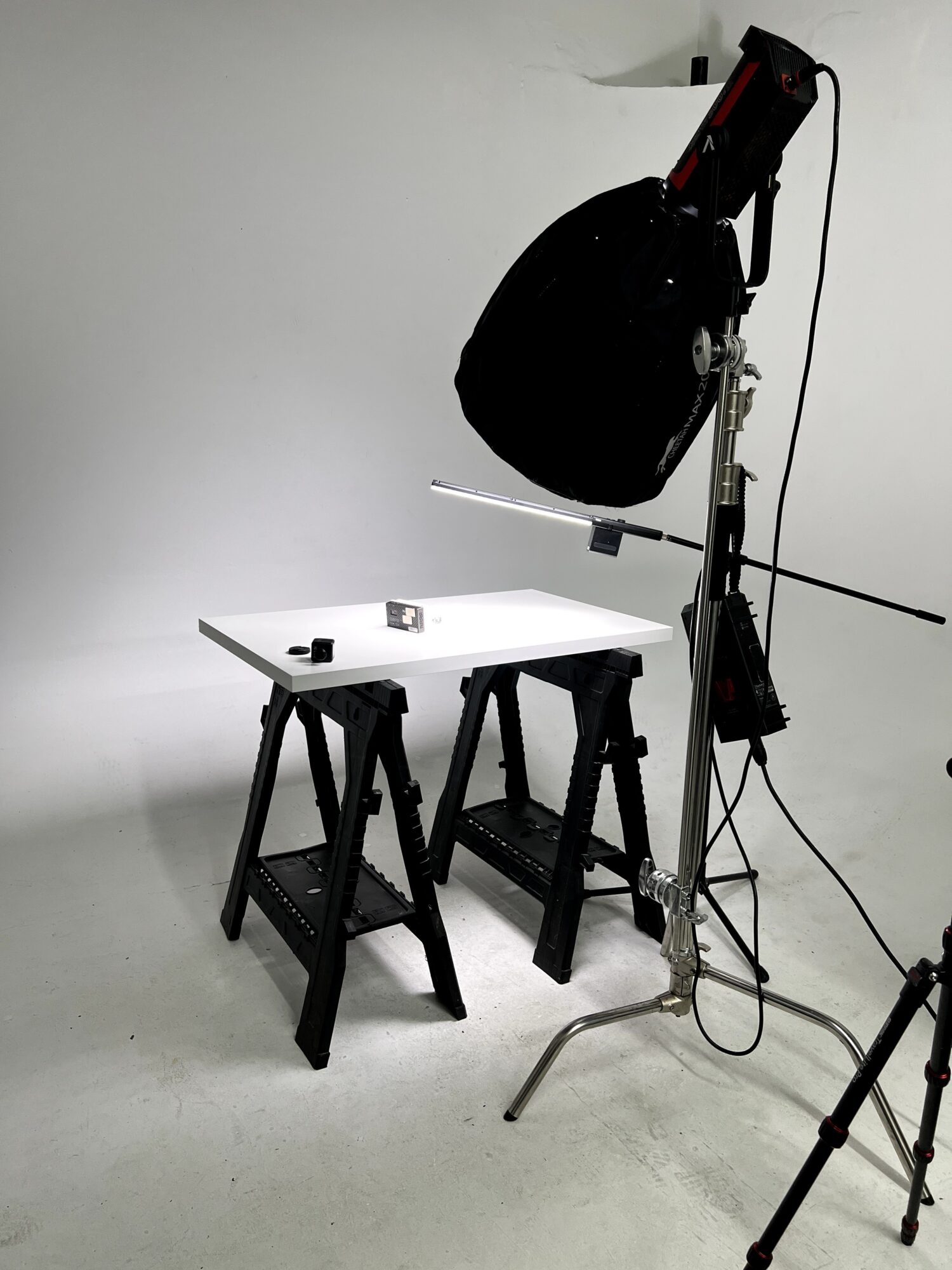 Photography studio setup with a large softbox, two black stools, and a white table against a plain background.