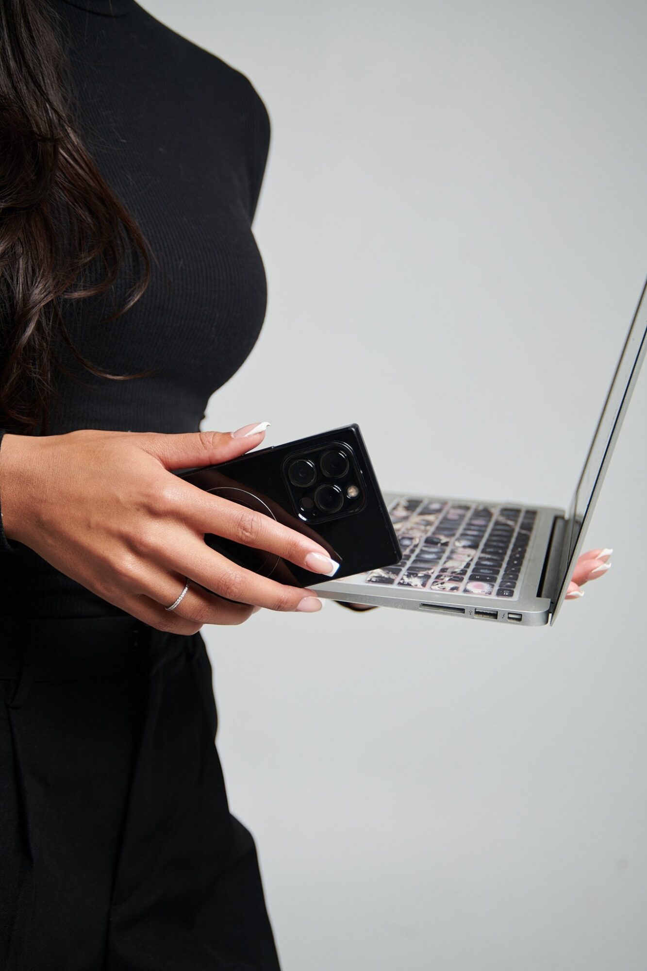 Person holding a smartphone and a laptop against a plain background.