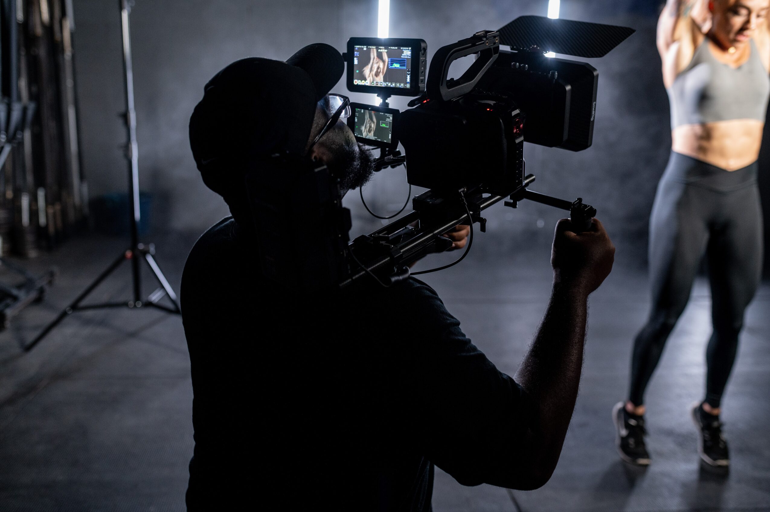 Person operating a professional video camera filming a woman in workout attire in a studio setting.