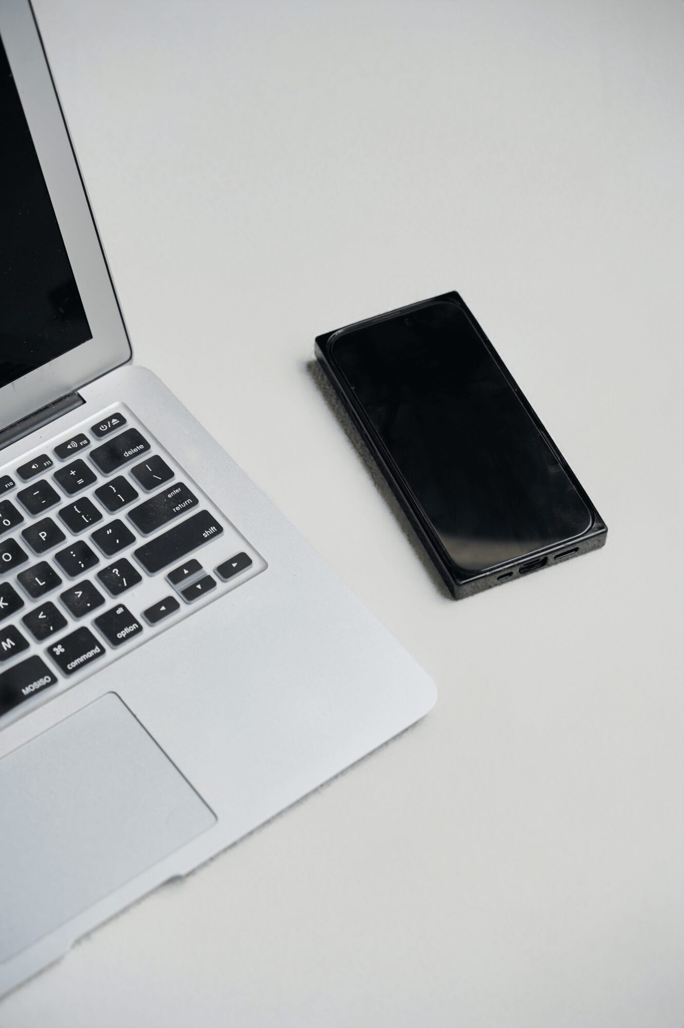 Laptop and a closed black smartphone on a white surface.