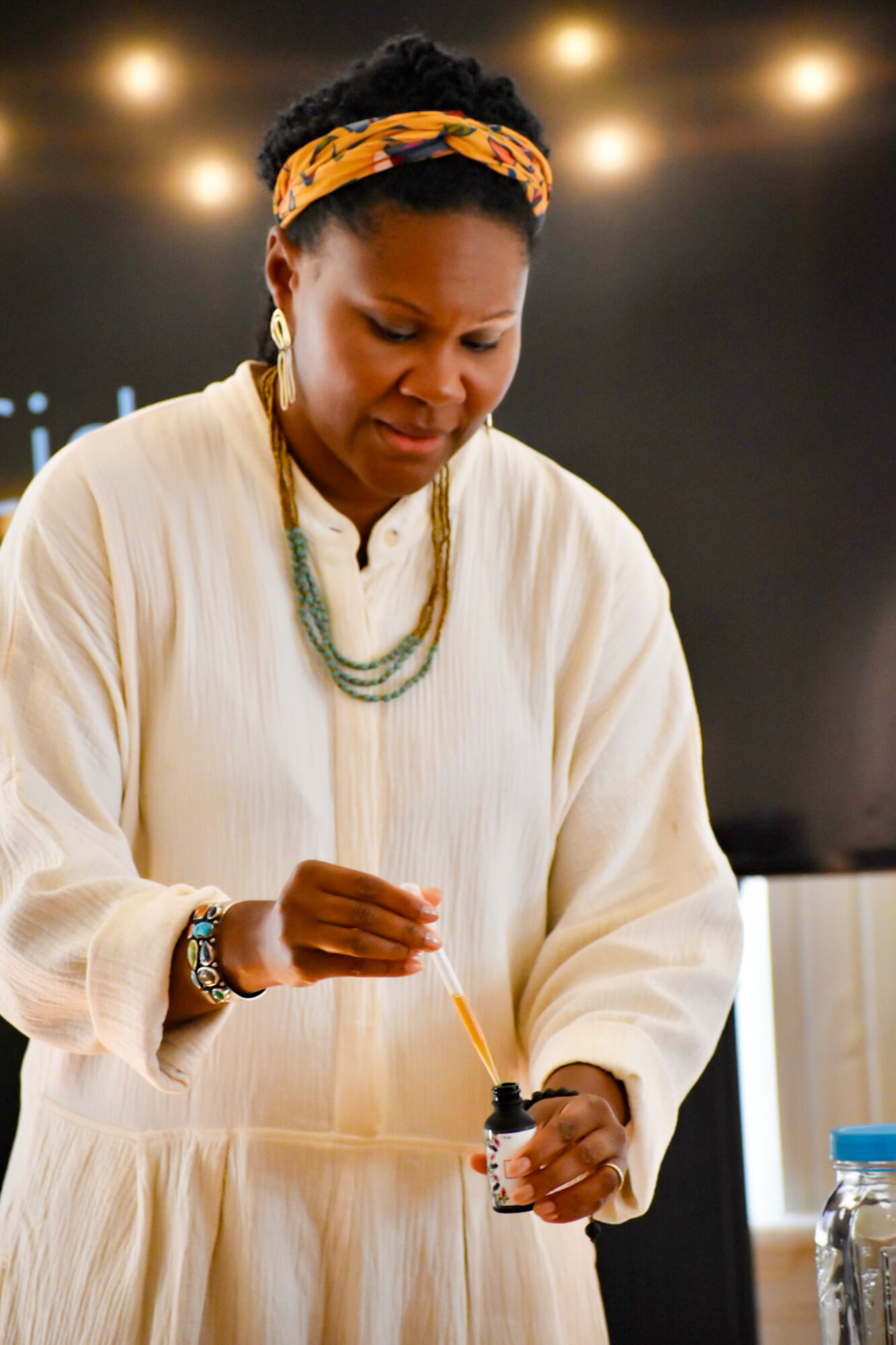 Woman with headband and jewelry holding a small object, focused on her task, indoors with dark background.