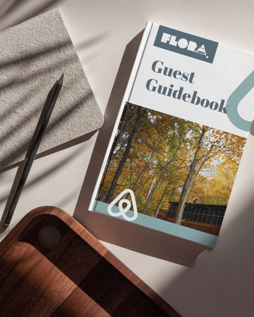 Guest guidebook titled 'FLORA' with a nature scene on the cover, placed on a white surface with a pen and notebook nearby.