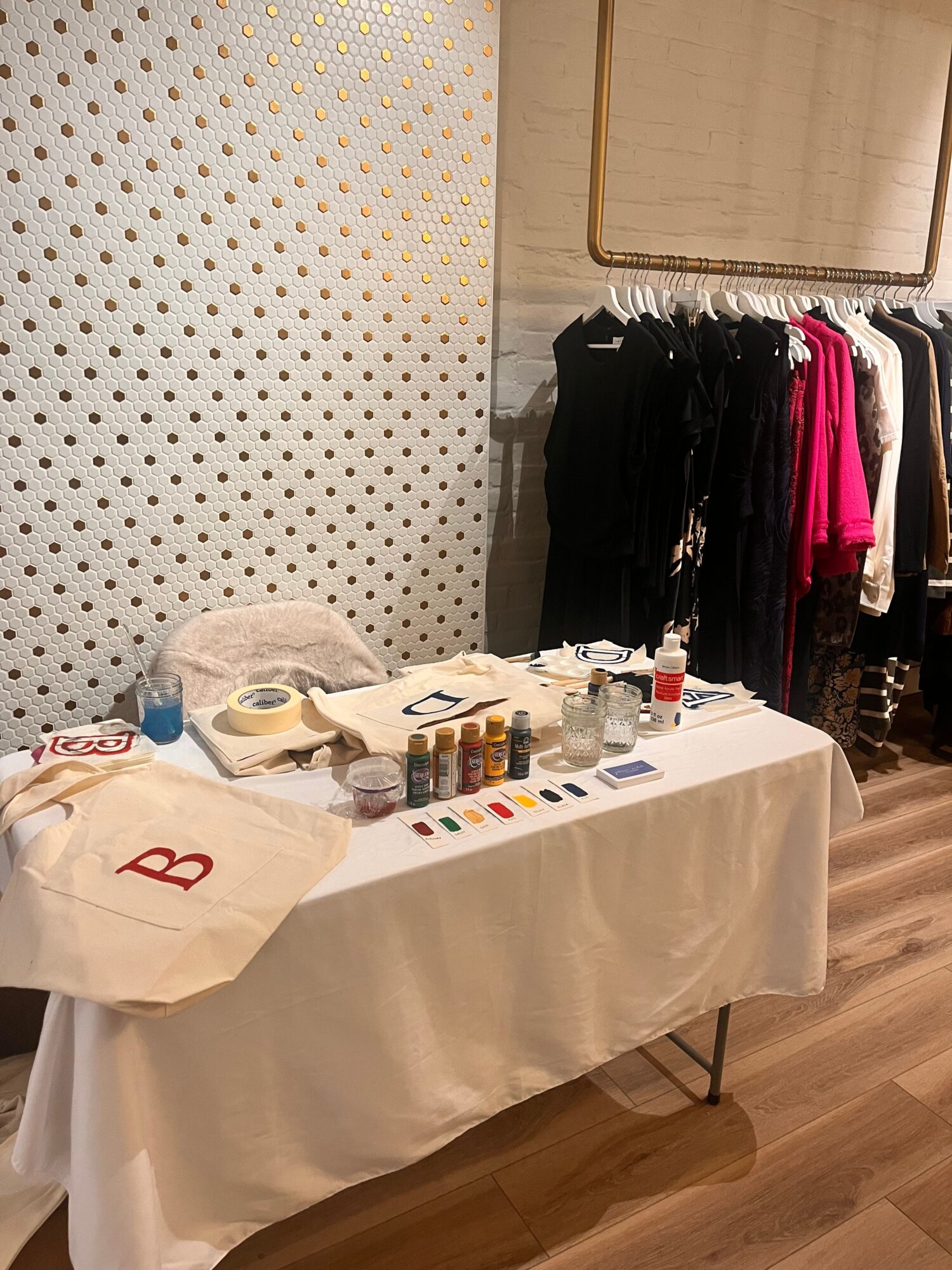 Table with nail polish bottles, tools, and a white bag, set in a room with clothing racks and polka dot wallpaper.