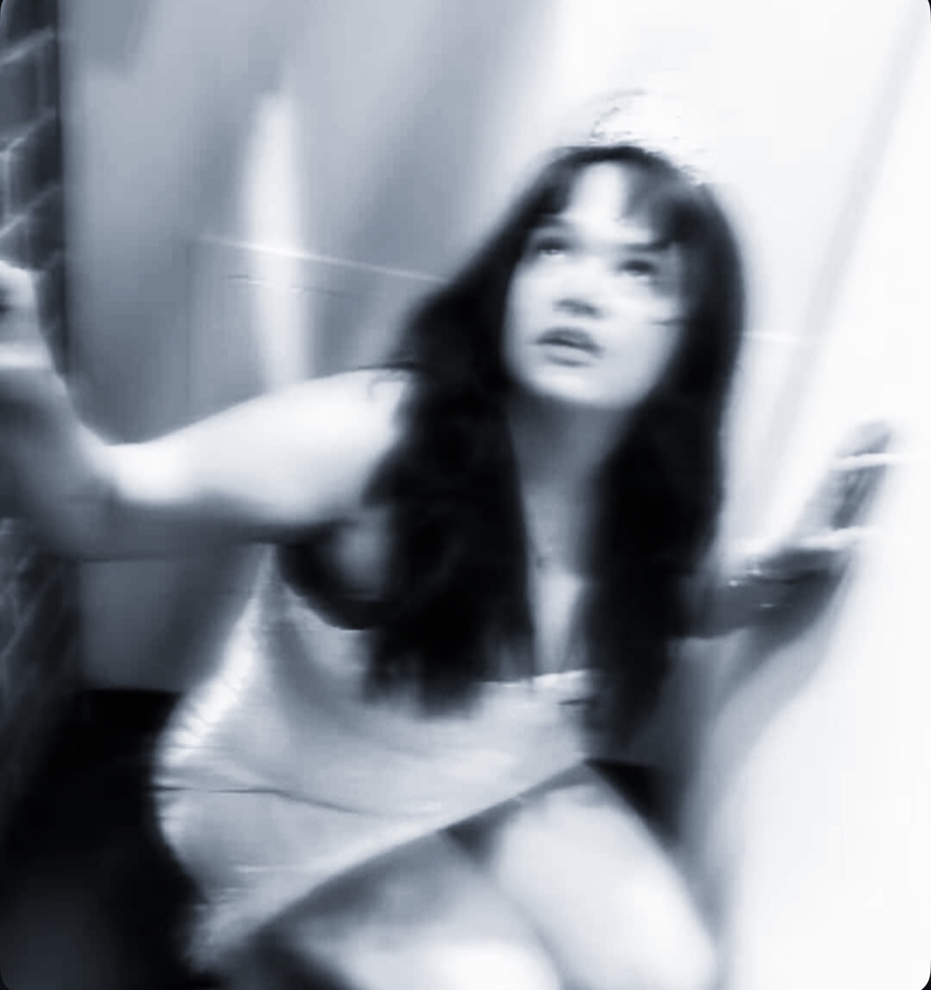 Blurry black-and-white photo of a woman with long dark hair, looking upward, in a confined space.