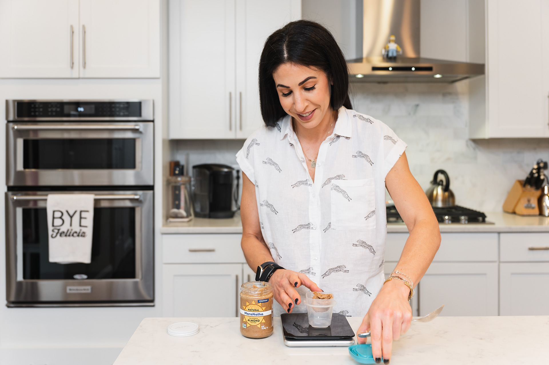 Woman in a white shirt preparing food in a modern kitchen with white cabinets and appliances.