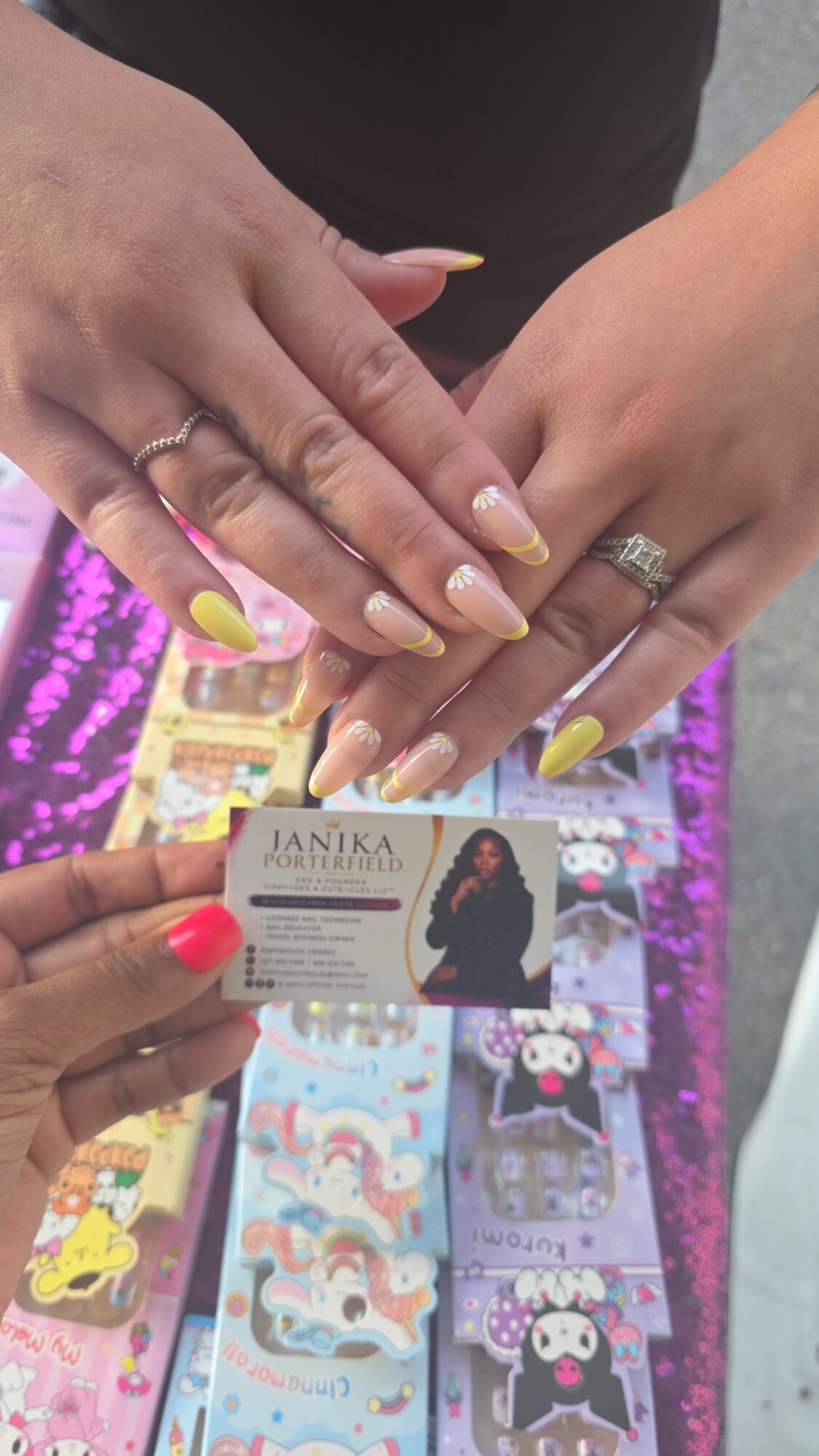 Two hands with rings and yellow nails touch over a colorful display of cards or stickers, with a person's hand holding a business card.