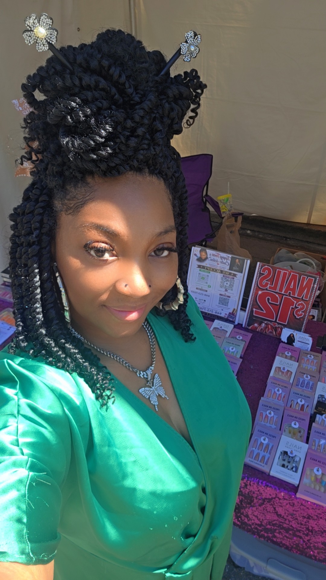 Woman with styled curly hair wearing a green top, smiling, standing indoors near a display of products.