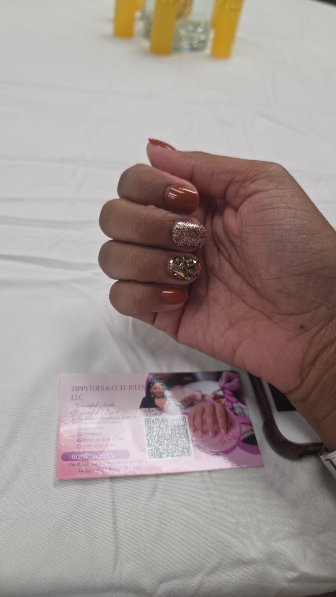 Hand with decorated nails resting on a surface with a pink card nearby.