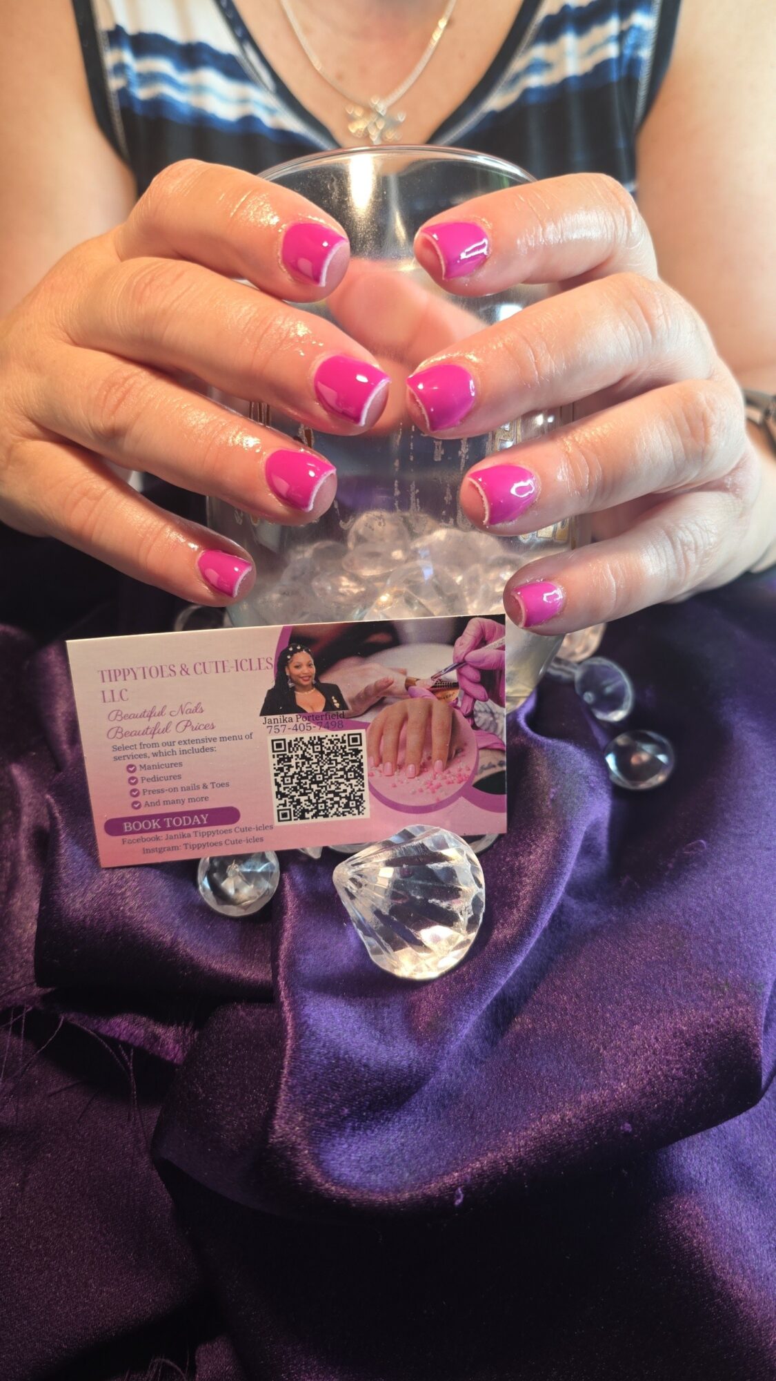 Person holding a glass with hands showing pink and purple nail polish, wearing a blue and white striped top, with a business card visible.
