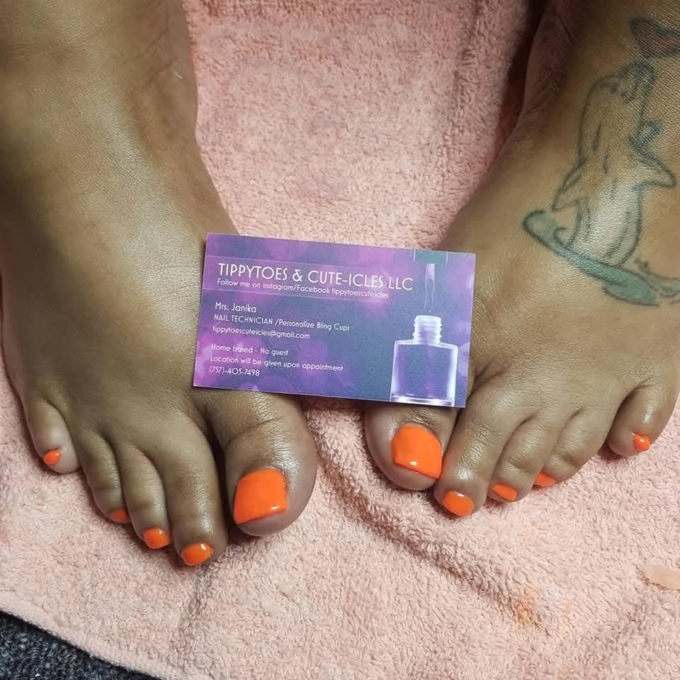 Feet with orange toenails resting on pink fabric, tattoo visible on right ankle, small purple box between toes, text on box.