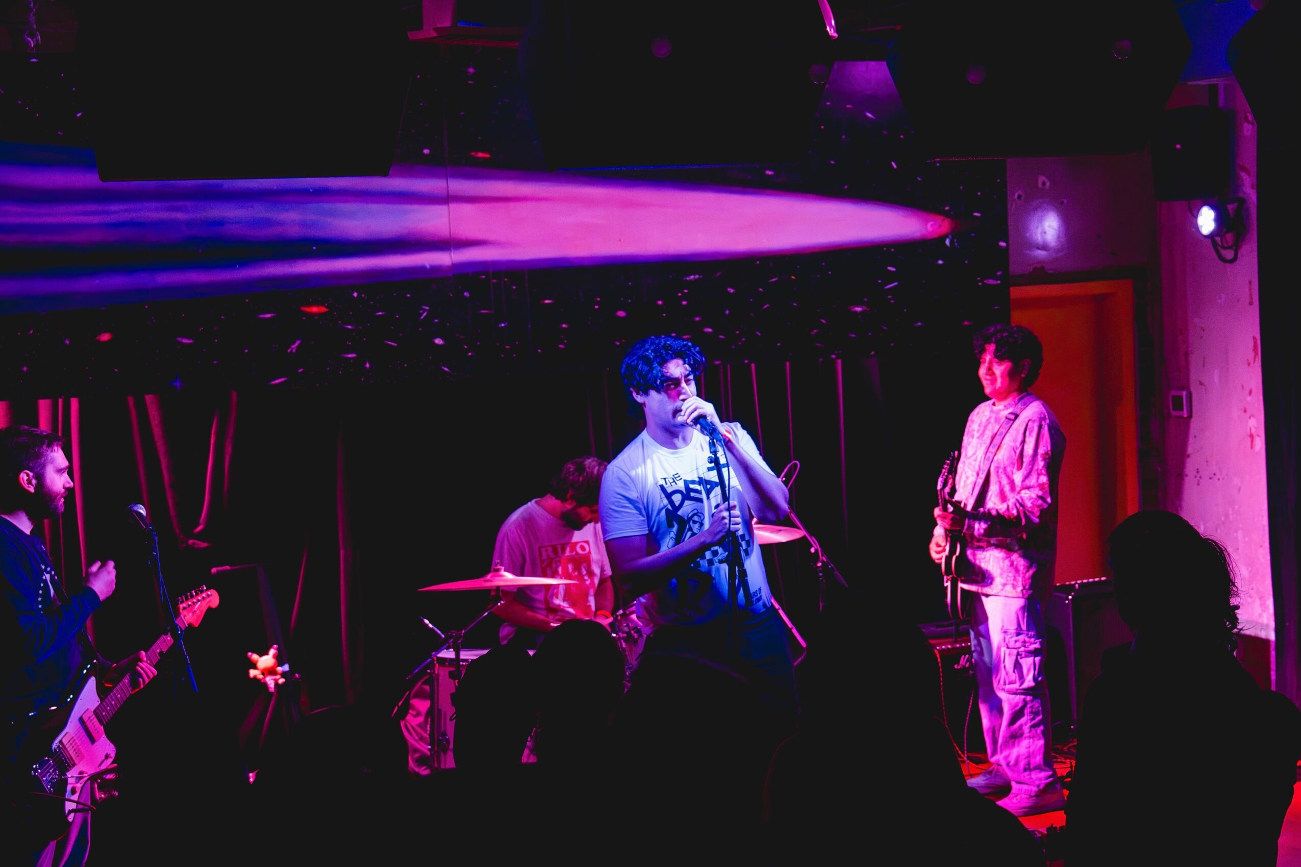 Band performing on stage with purple lighting, singer with microphone, and audience silhouettes visible.