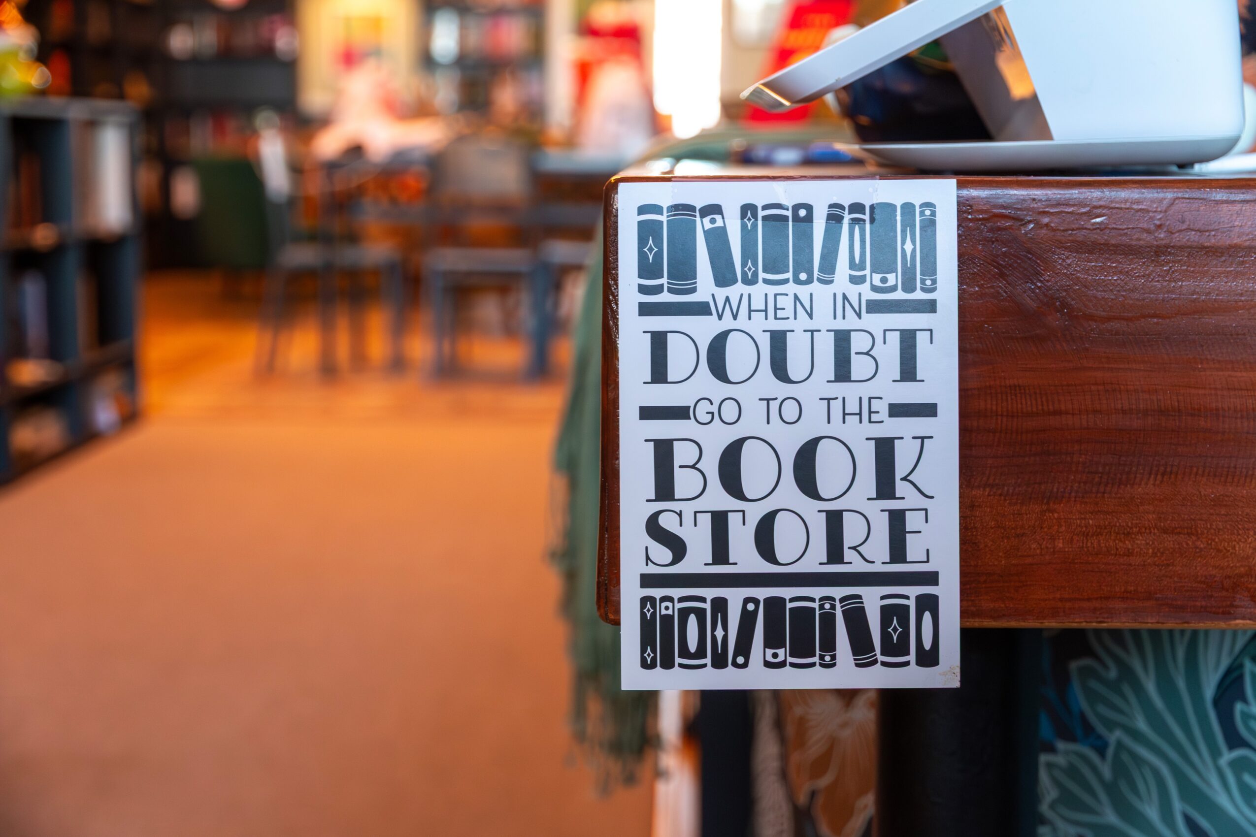 Sign with text about doubt and going to the bookstore, hanging on a wooden surface in a bookstore or library, blurred background