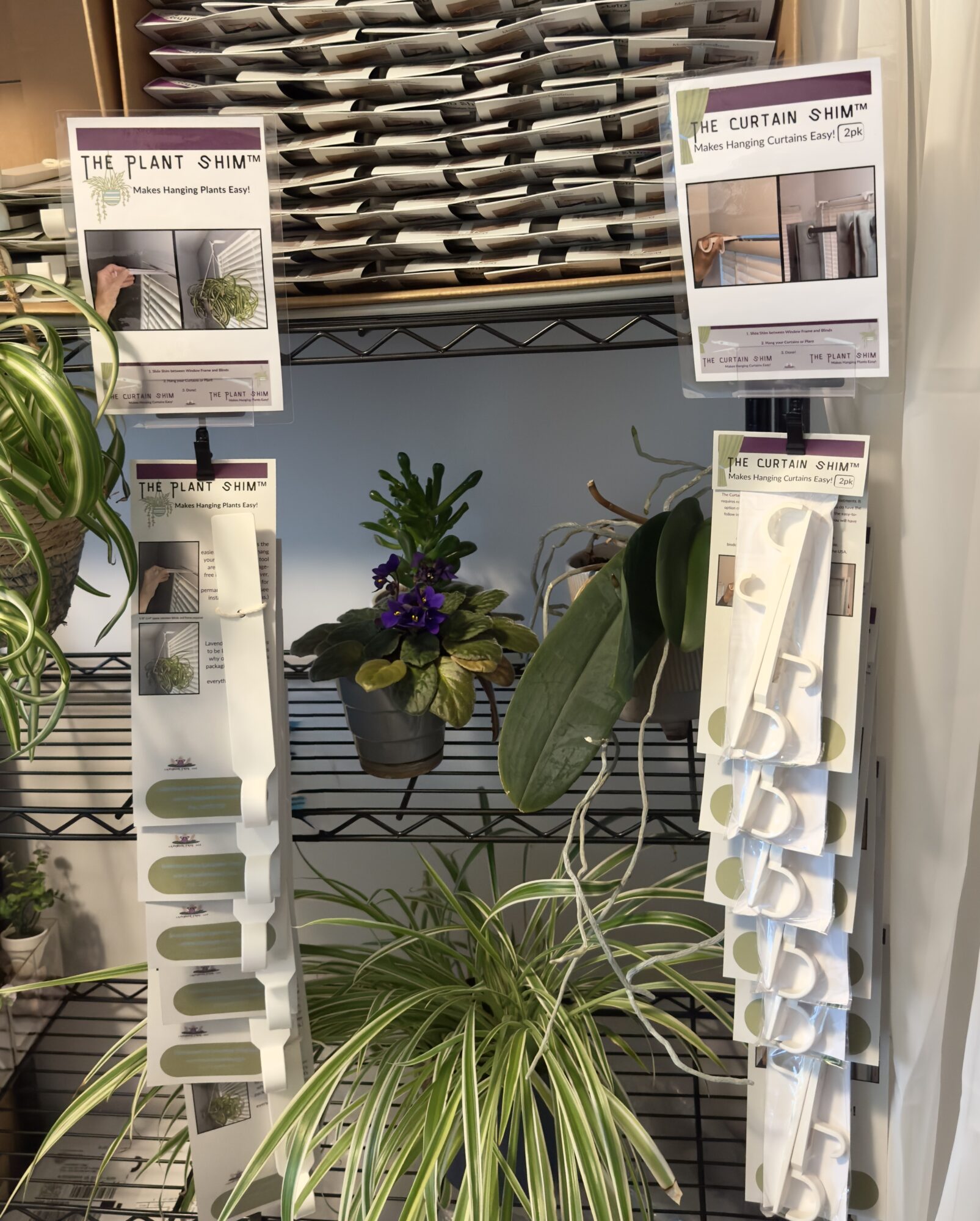 Display of plant care products and potted plants on a metal shelf, with plant samples and informational signs.