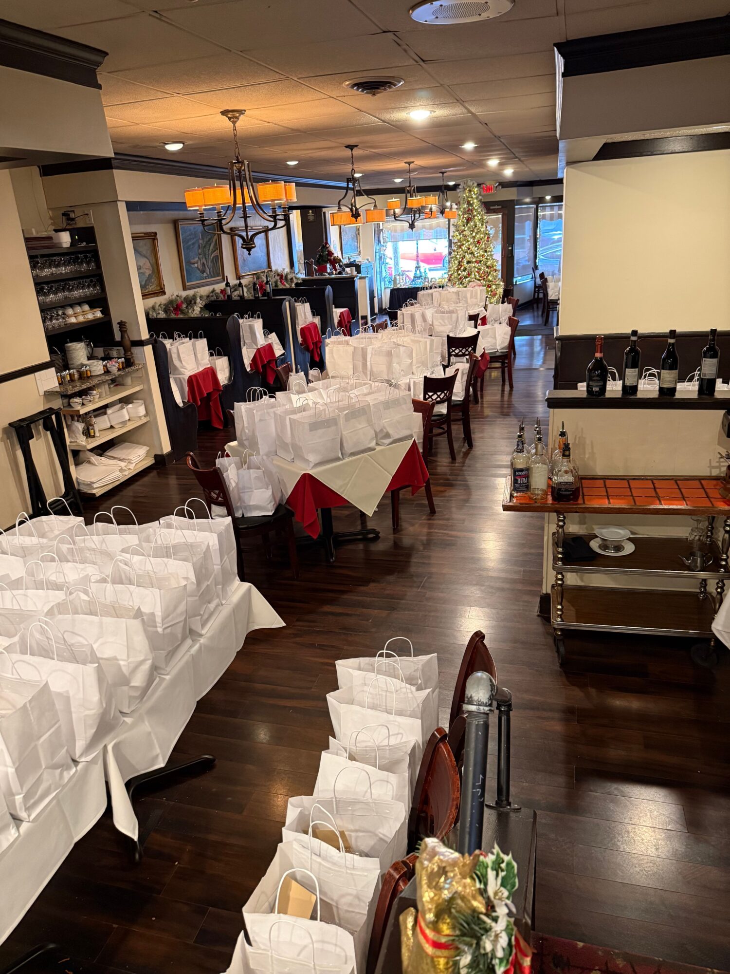 Restaurant dining area with tables set with white tablecloths, napkins, and flowers, ready for guests, with a bar in the background.