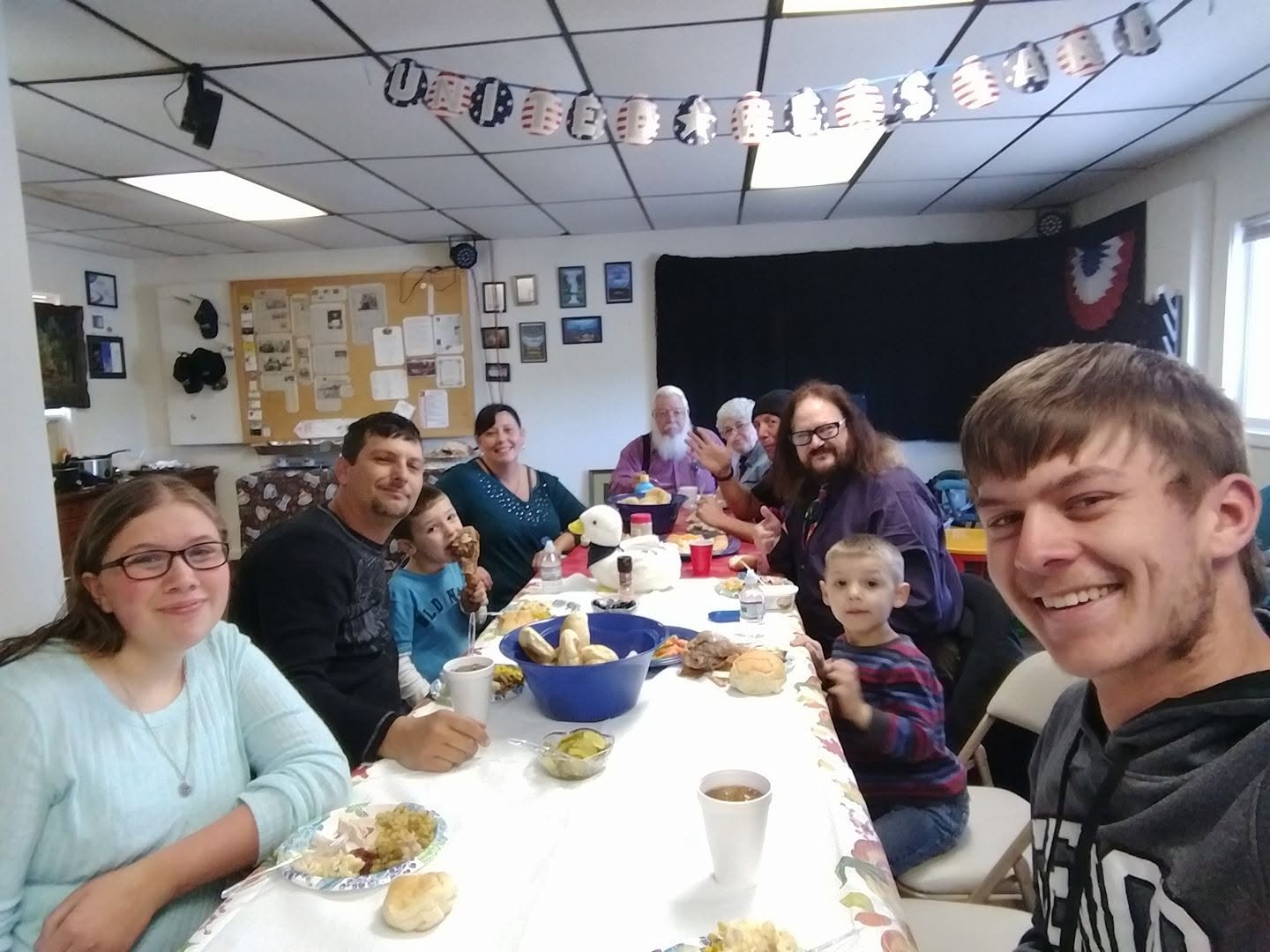 Group of people gathered around a table with food, celebrating indoors with decorations and a blackboard in the background.