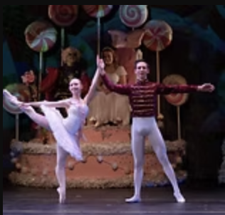Two ballet dancers perform on stage with colorful candy-themed decorations in the background.