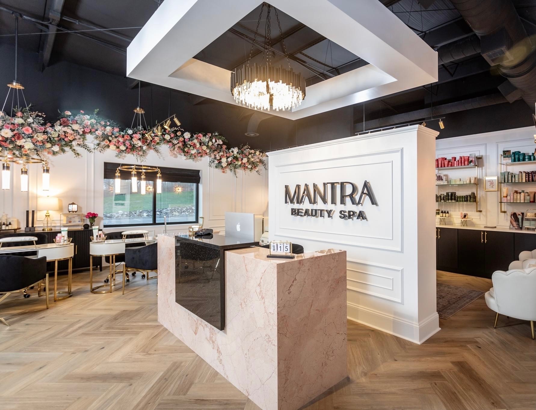 Beauty spa reception area with floral decorations, a reception desk, and seating, featuring a chandelier and modern decor.