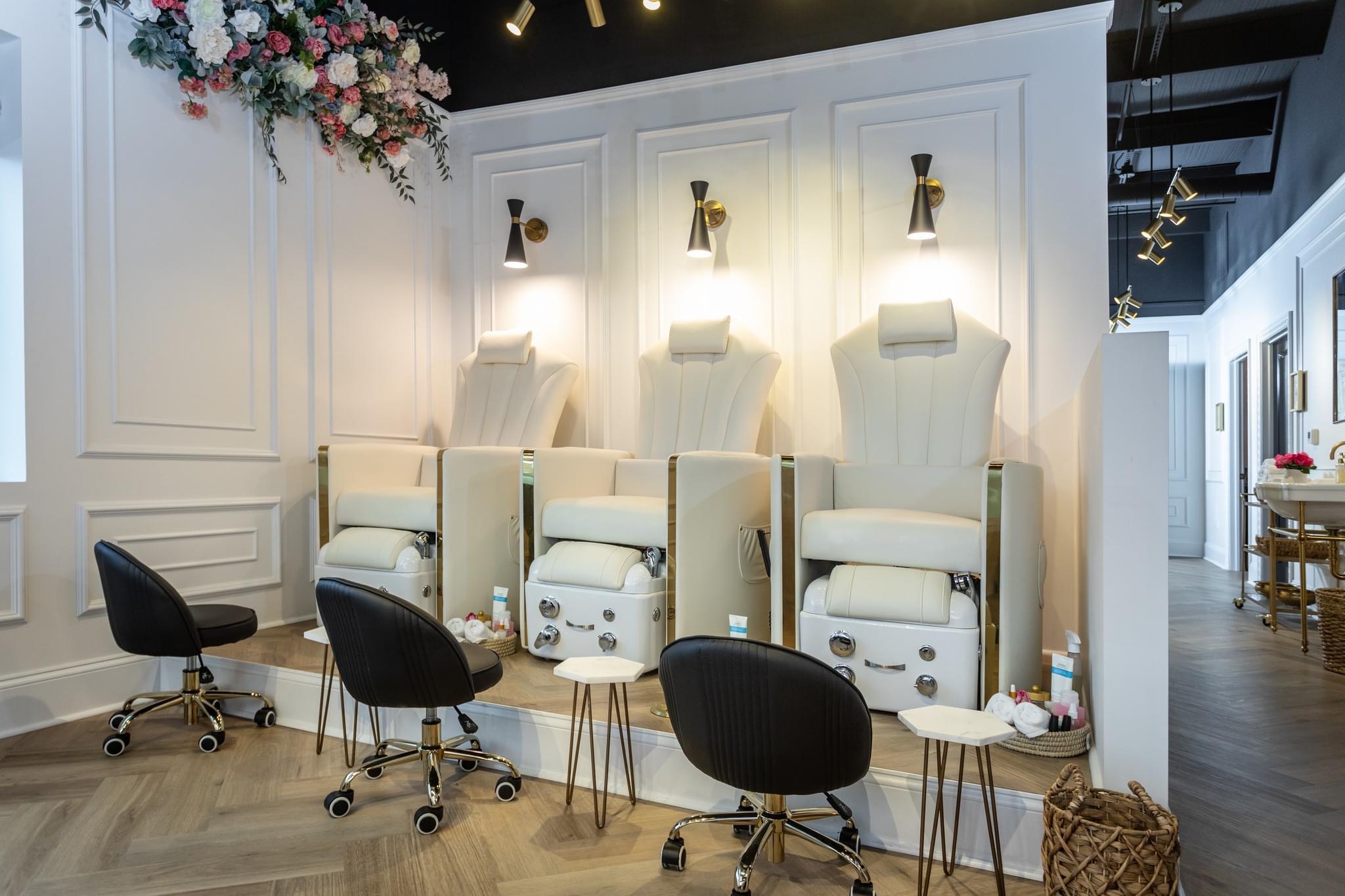 Nail salon with four pedicure chairs, three black stools, and a white wall with floral decoration, in a modern space.