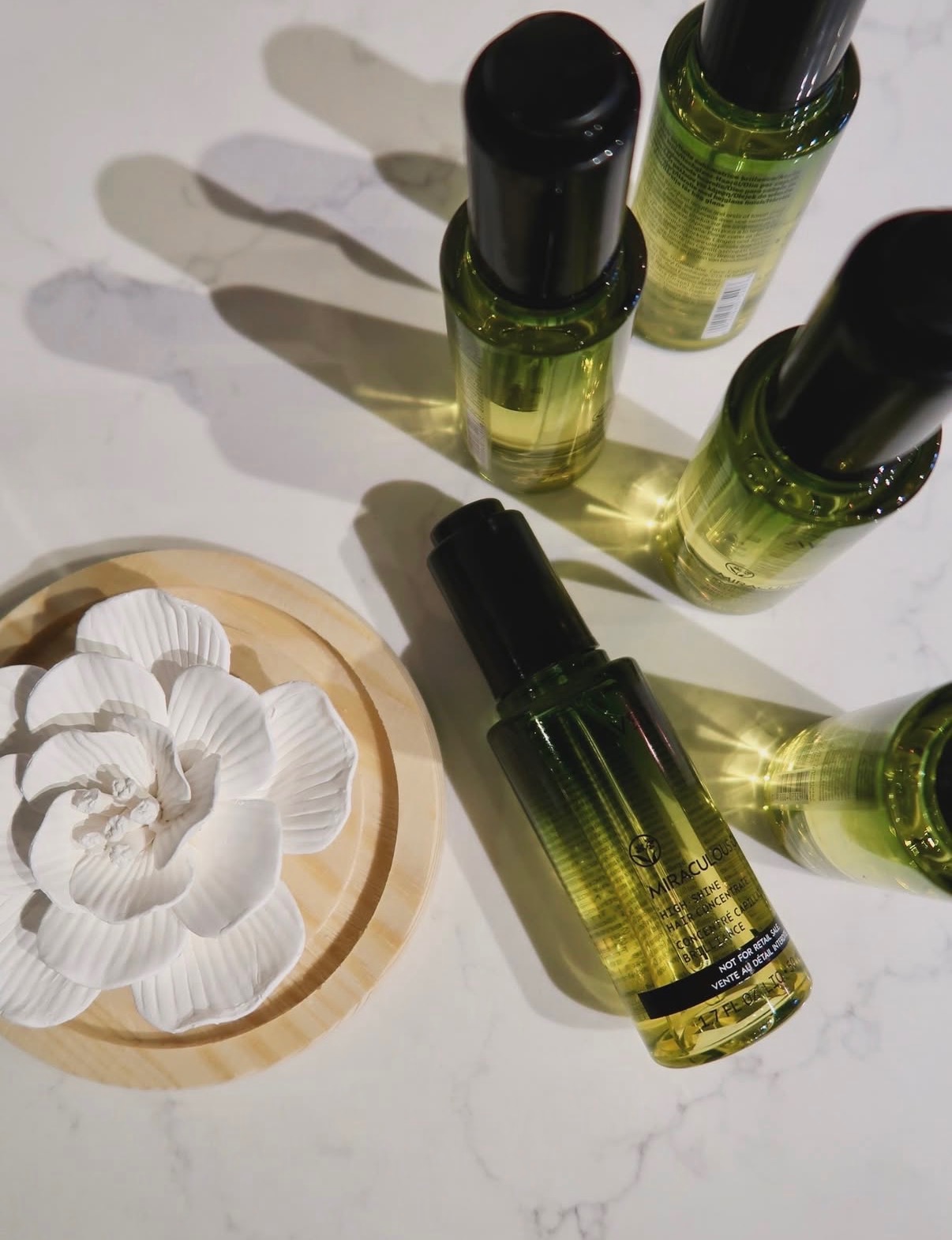 Six small bottles with black caps and yellow liquid inside, arranged on a white surface, with a white decorative flower in a wooden dish.