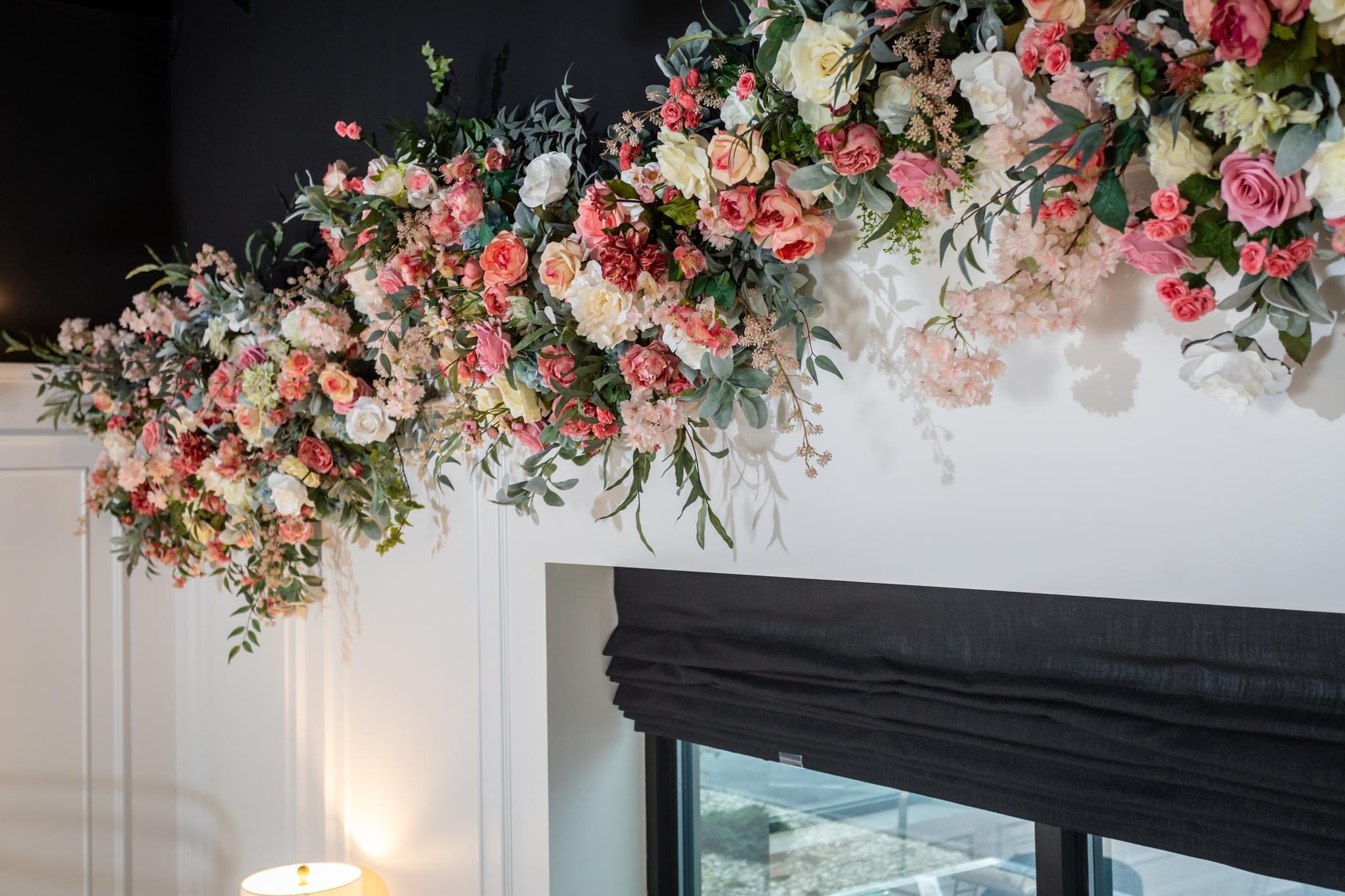 Close-up of a floral arrangement with pink, white, and red flowers above a window with a black curtain.