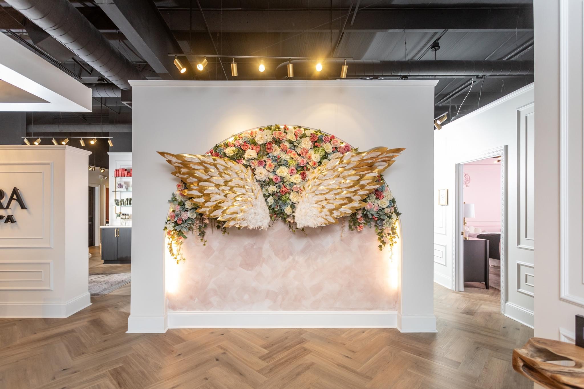 Wall display with floral arrangement and golden wings, illuminated by spotlights, in a modern interior space.