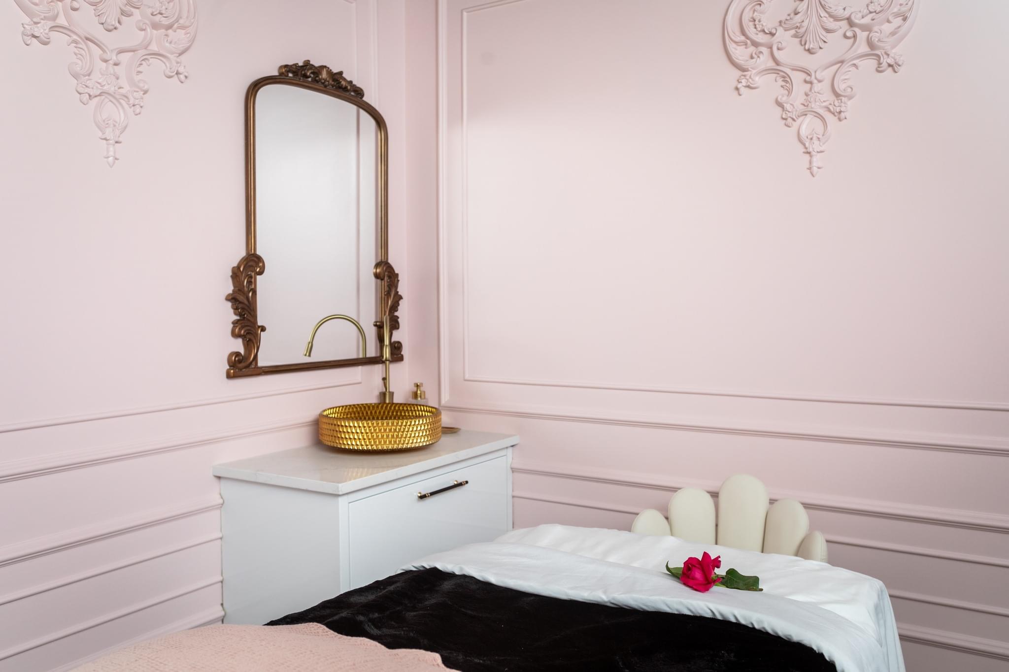 A bedroom with pink walls, a white bed with a black blanket, and a white dresser with a mirror above it.