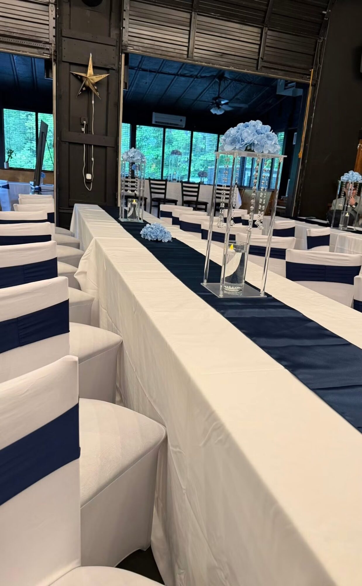 Long table with white tablecloth, navy runner, tall candles, and floral arrangements in a decorated event space.