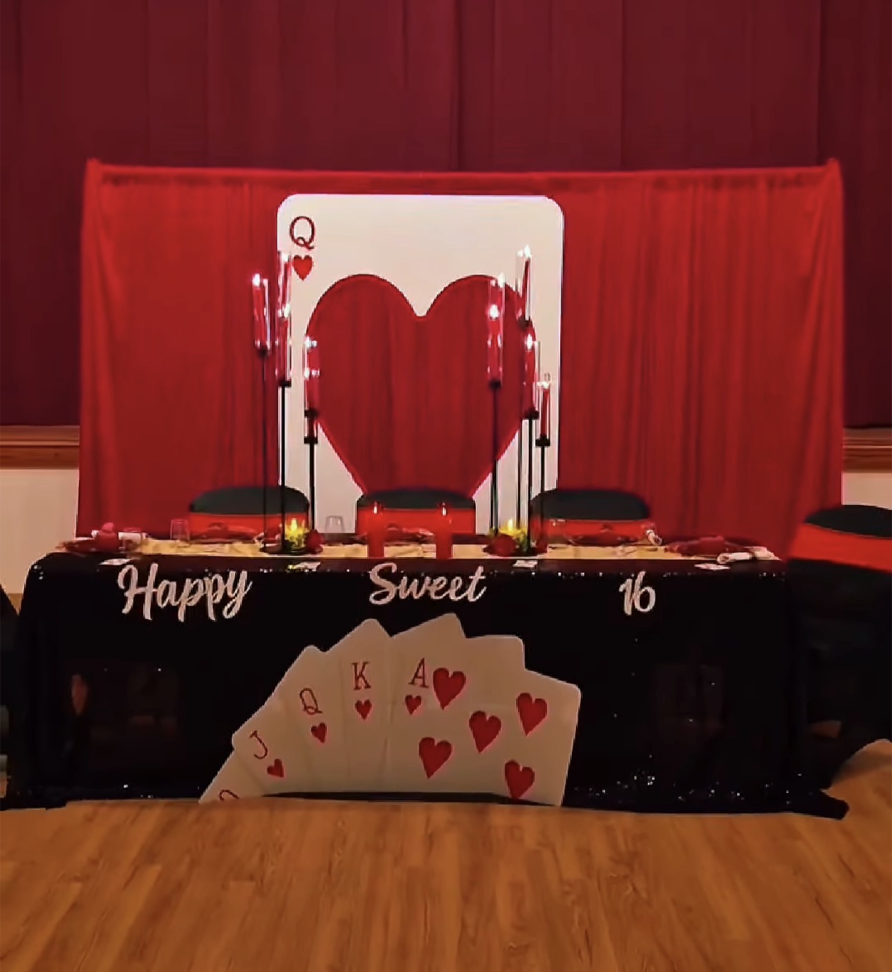 Table with playing cards, heart-shaped decoration, and a red curtain backdrop for a celebration.