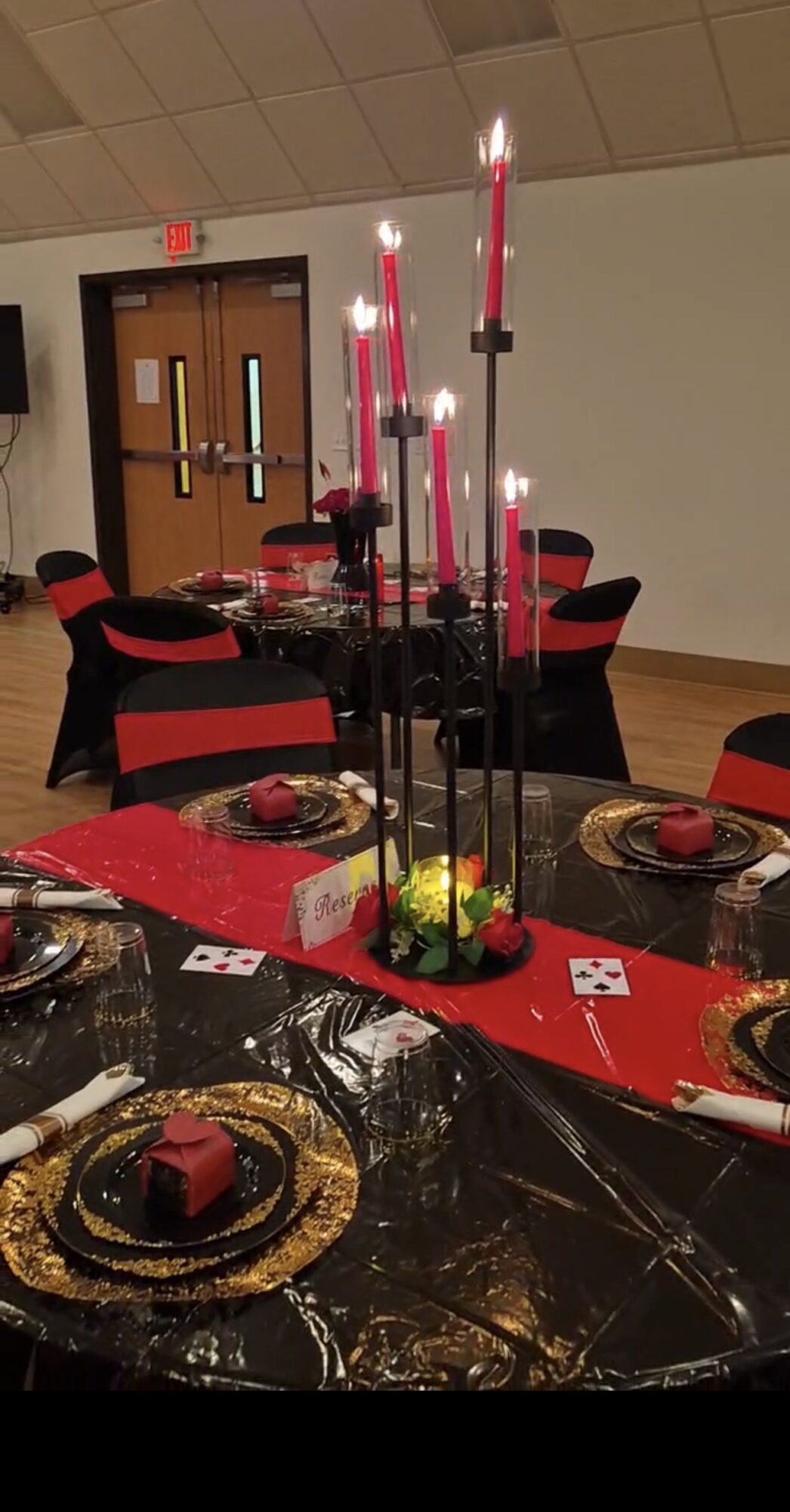 Table decorated with black and red tableware, a tall black candle holder with pink candles, and a red table runner.