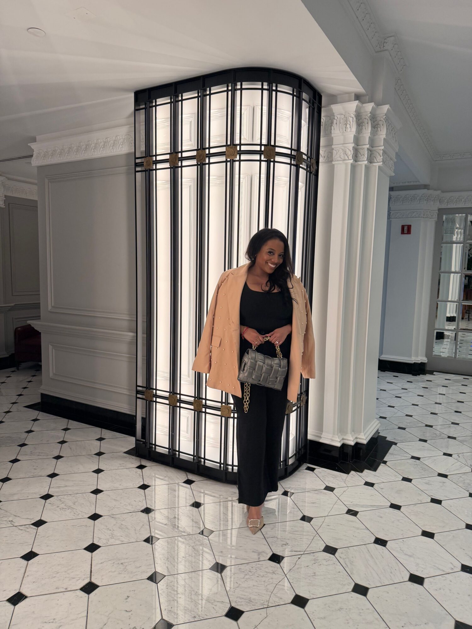 Woman standing in front of a large metal cage with black bars, in a room with black and white tiled floor.
