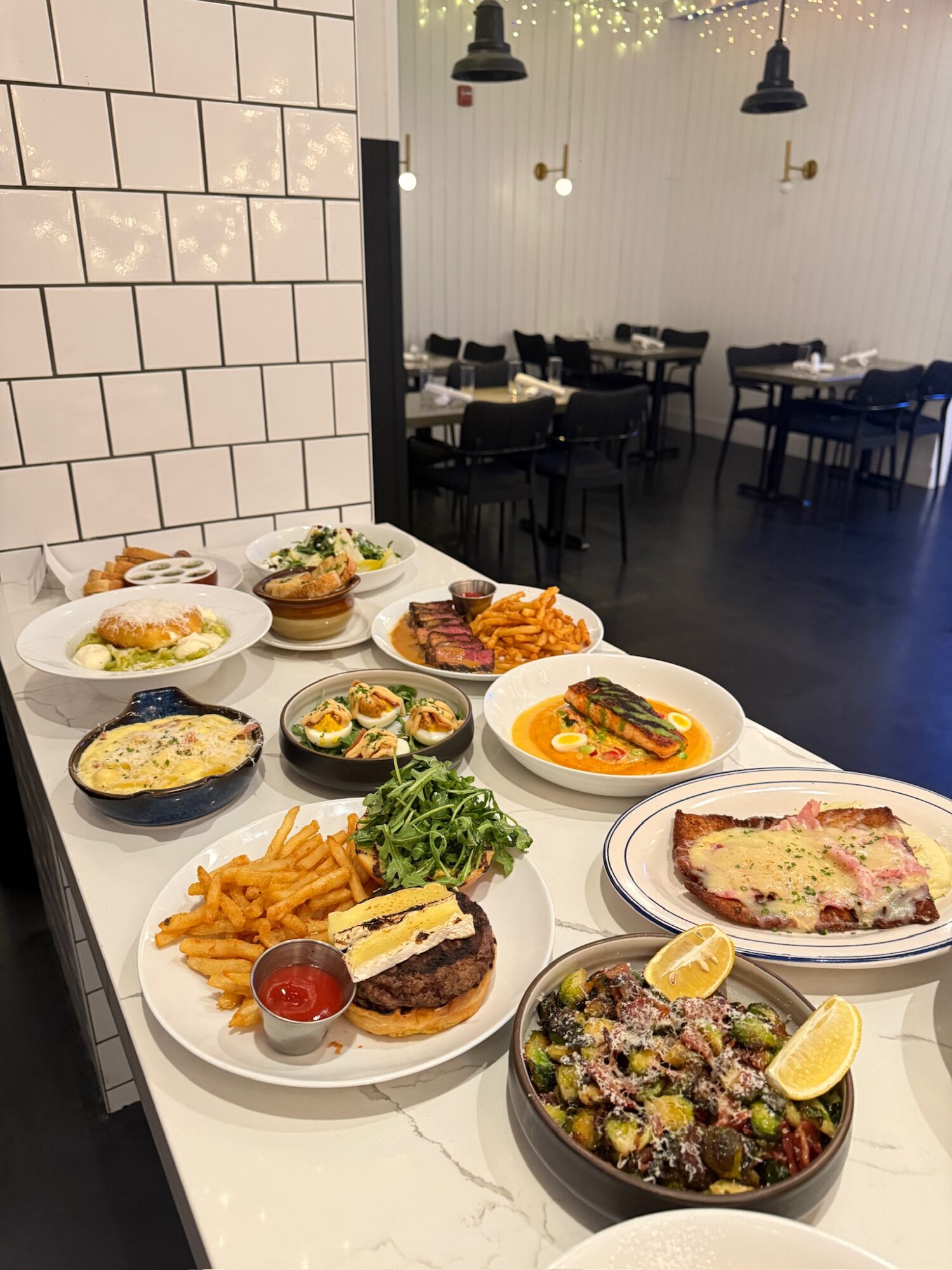 Assorted dishes on a white counter in a restaurant, with tables and chairs in the background.