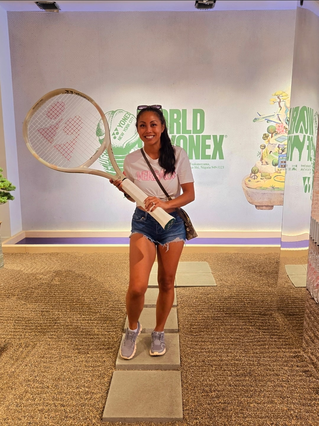 Young girl holding a tennis racket and a book, smiling, standing on a platform in front of a World Tennis logo backdrop.