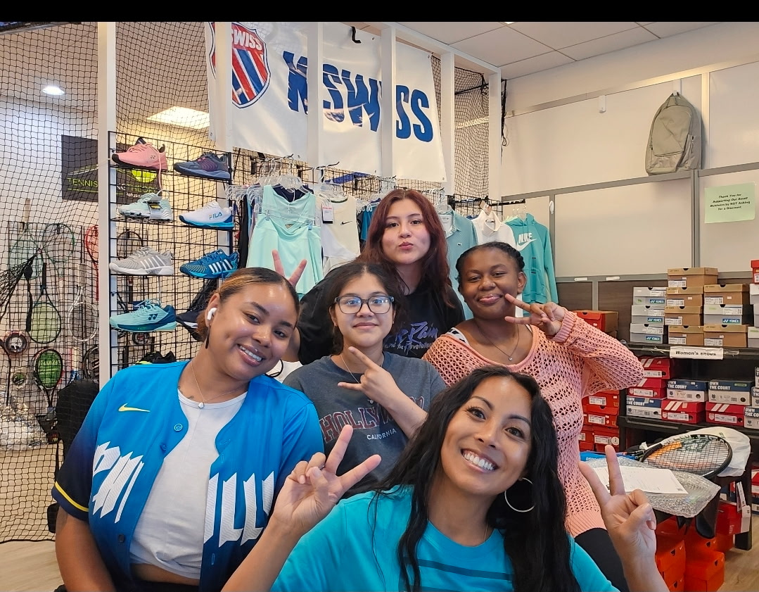 Five women posing inside a store, some making peace signs, with clothing and shoes in the background.