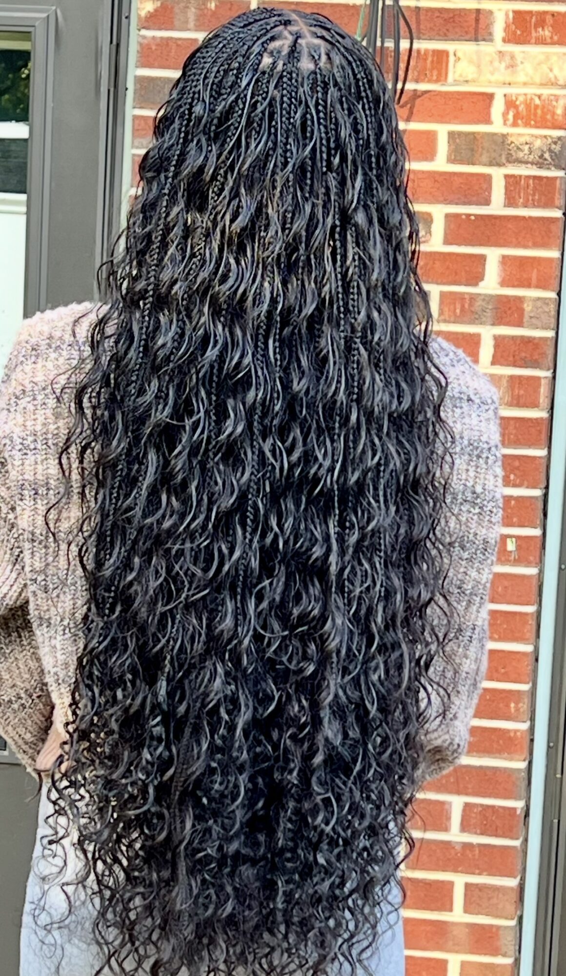 Person with long, curly, black hair standing outdoors near a brick wall, back view.