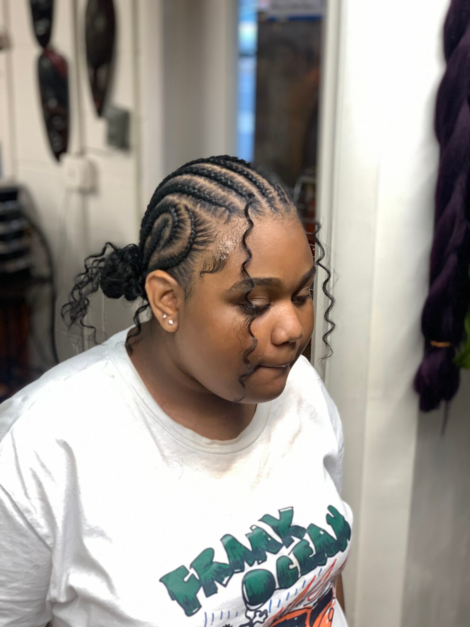 Young girl with braided hairstyle, wearing a white T-shirt, looking down, in a salon setting.