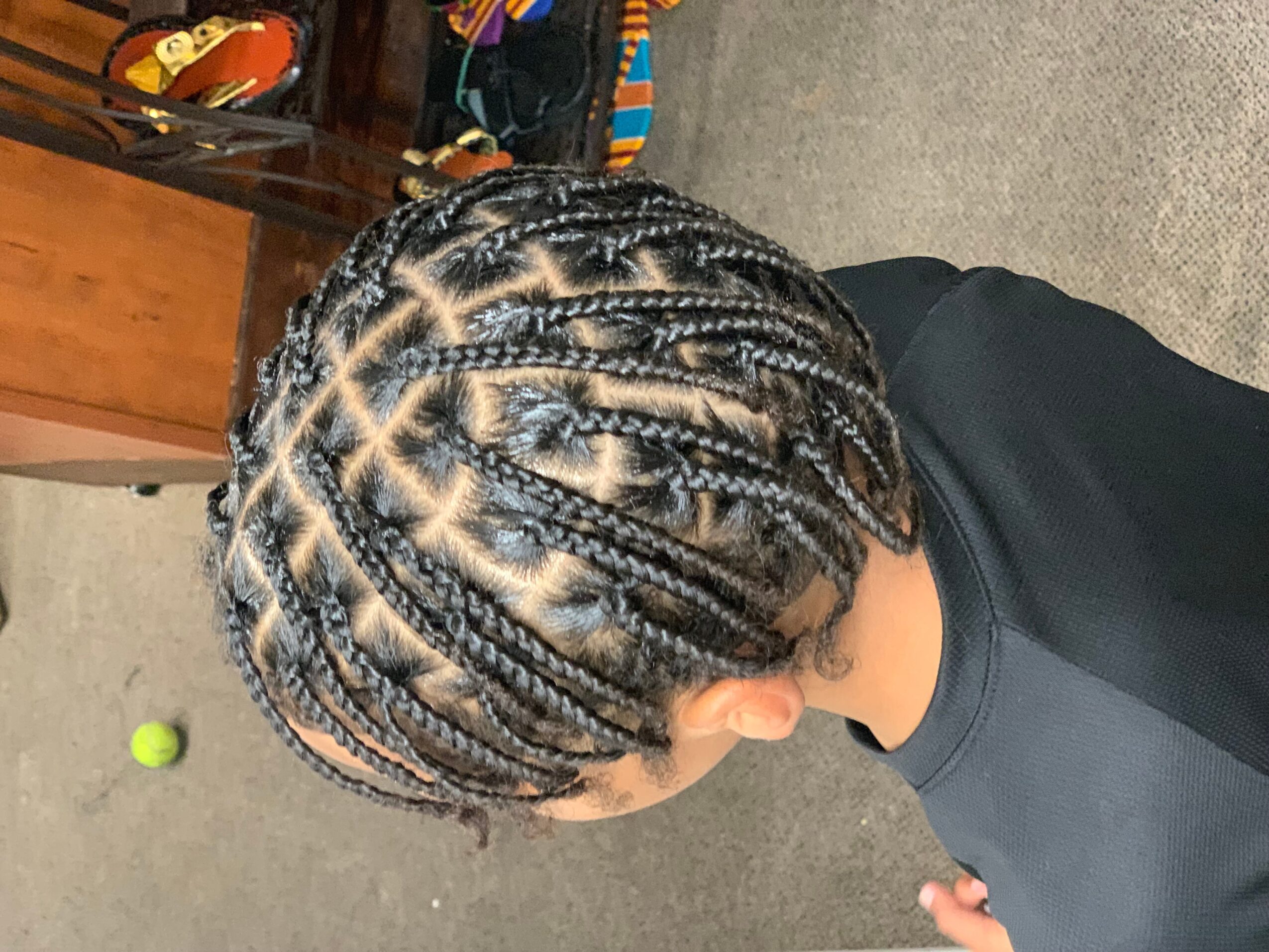 Top view of a person with braided hair styled in cornrows, wearing a black shirt, indoors.