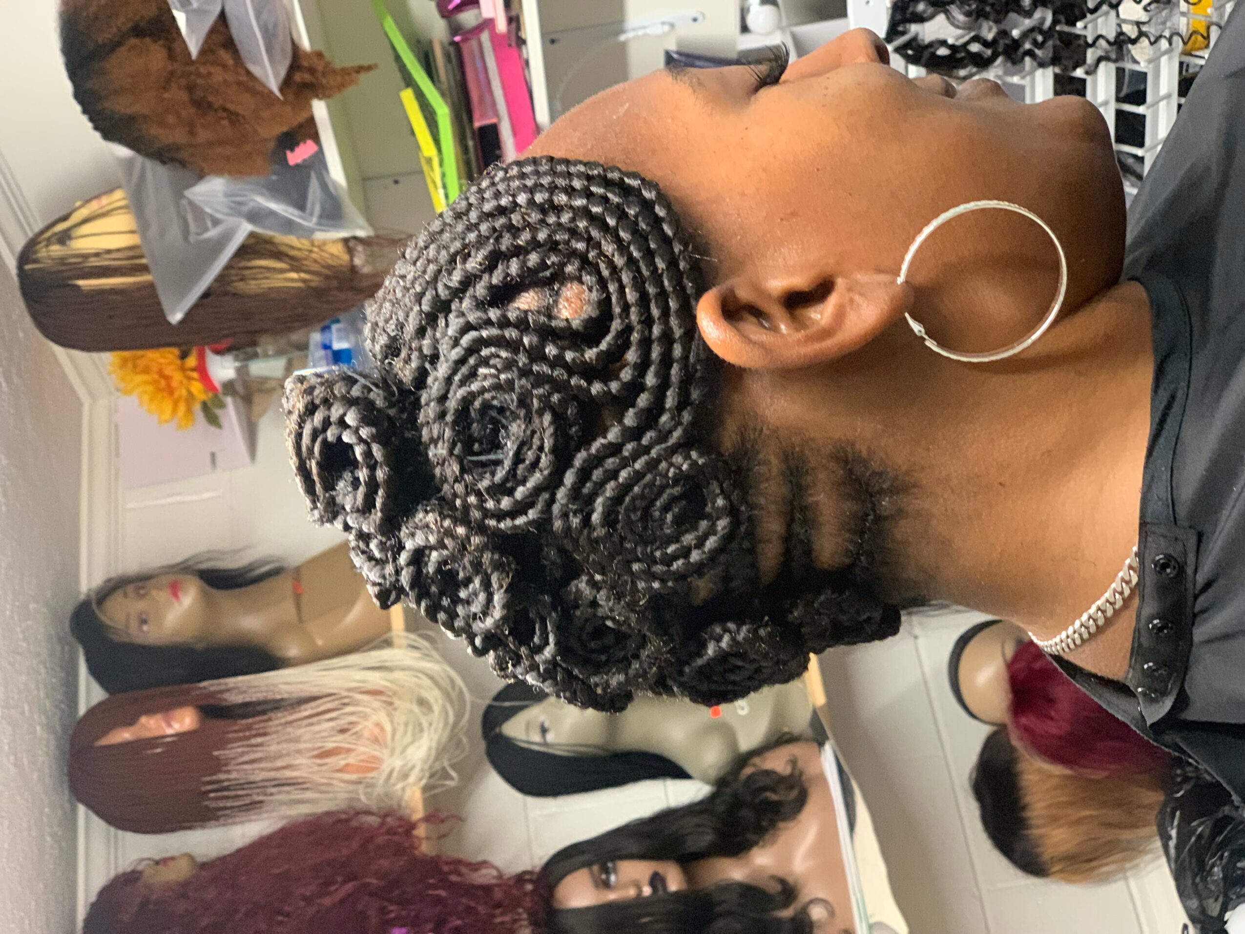 Side view of a woman with intricately styled braided hair, wearing hoop earrings, in a salon setting.