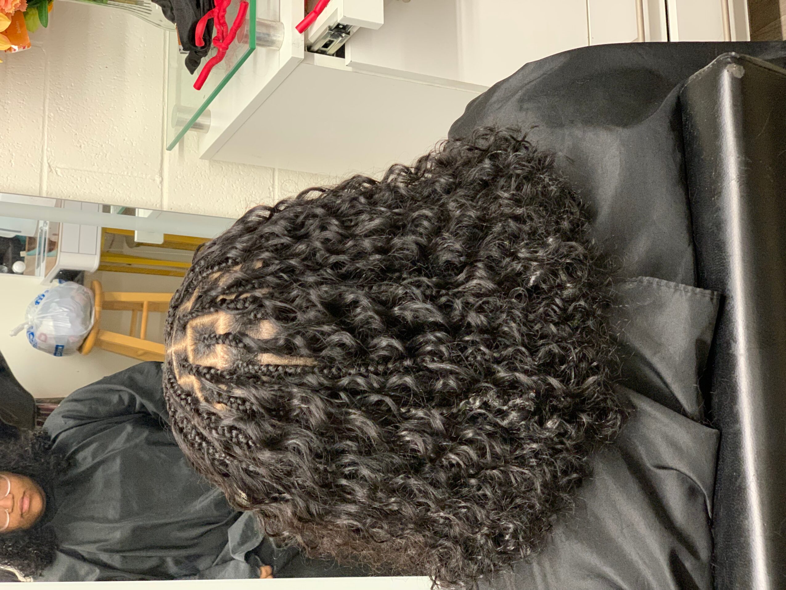 Top view of a person with curly hair sitting in a salon chair, with salon equipment visible in the background.