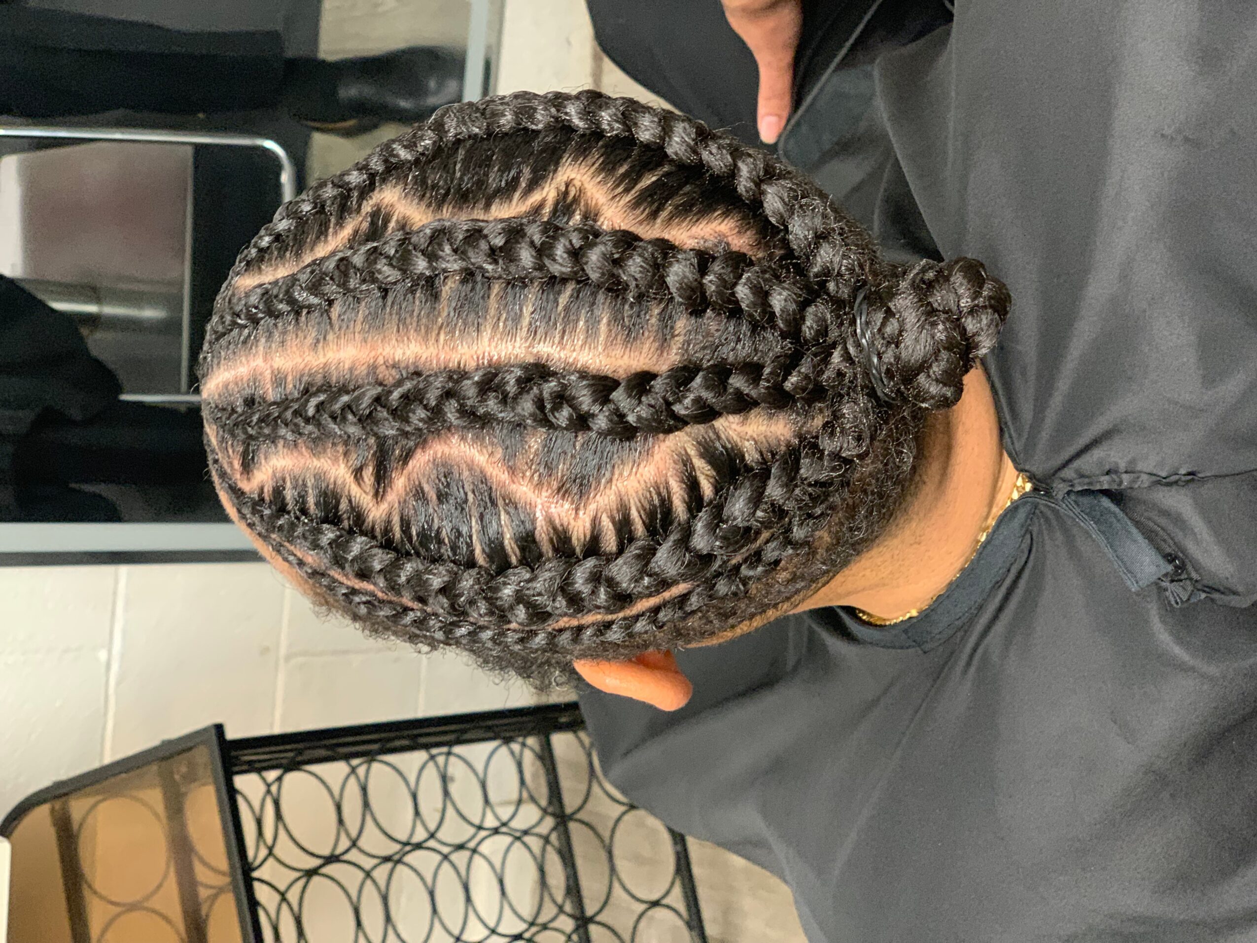Top view of a person's head with neatly braided hair styled into multiple cornrows, gathered into a bun at the back.