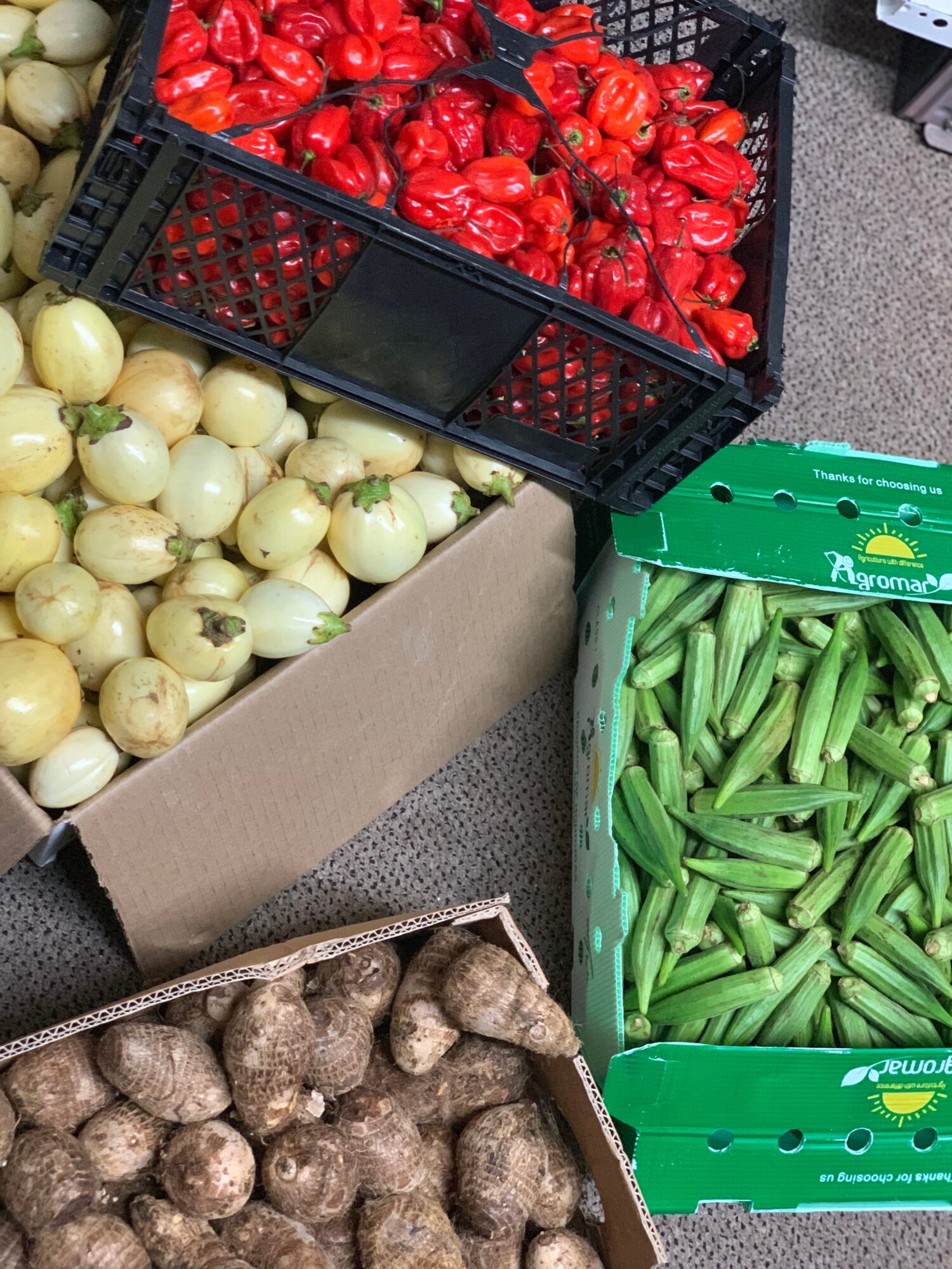 Crates of red peppers, green beans, onions, and potatoes displayed at a market stall.