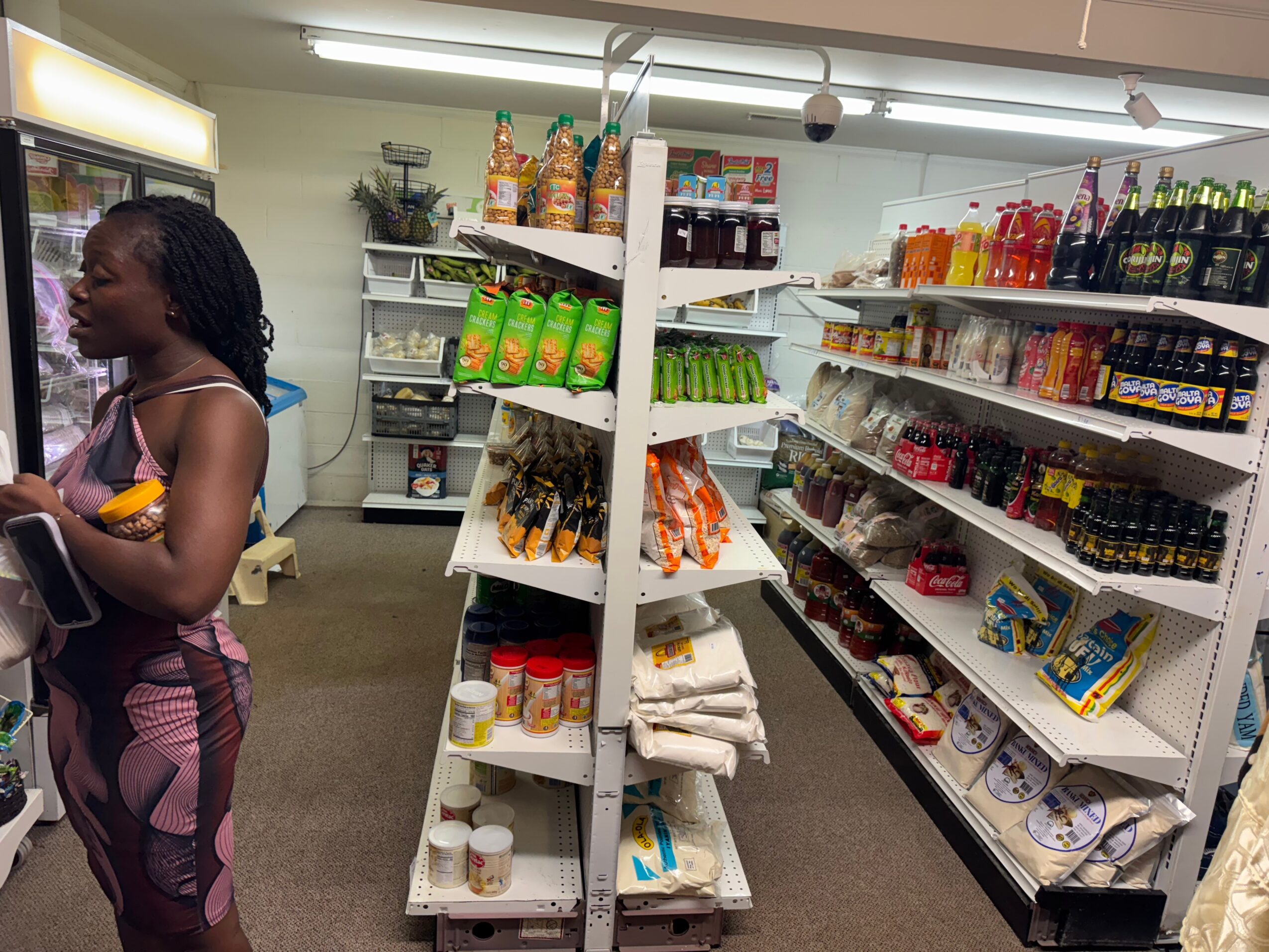 A woman shopping in a grocery store aisle with shelves stocked with snacks, drinks, and household items.