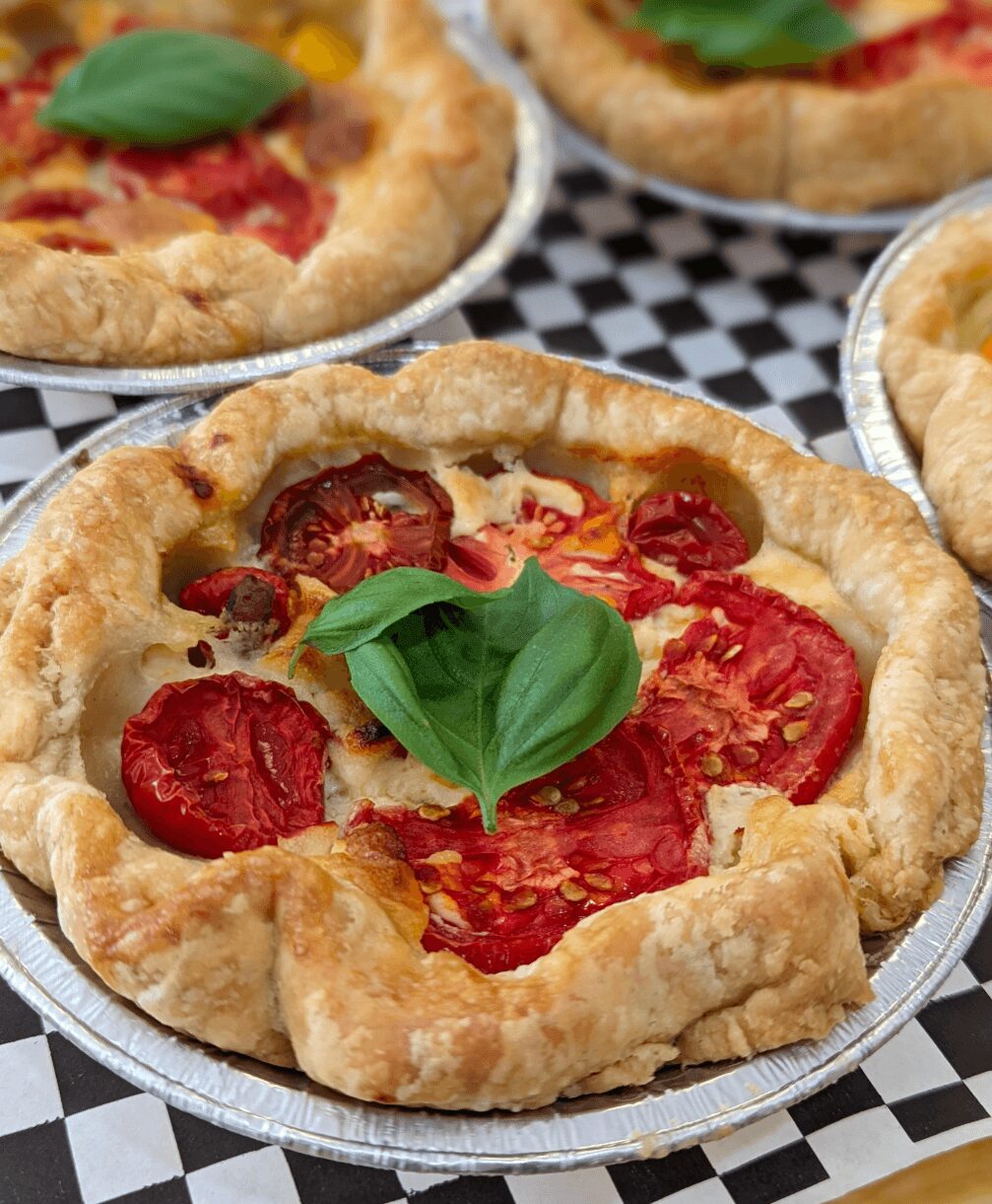 Close-up of a pepperoni pizza with basil leaves on top, in a foil container, on a checkered surface.